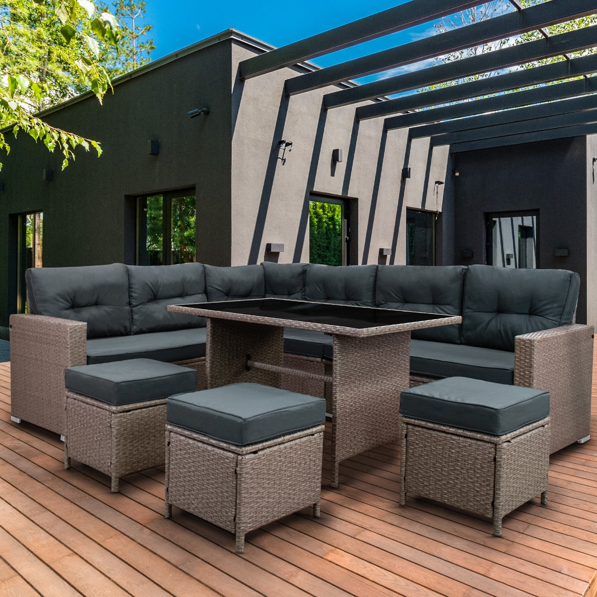 Sofá modular gris con mesa en terraza de madera frente a casa moderna.