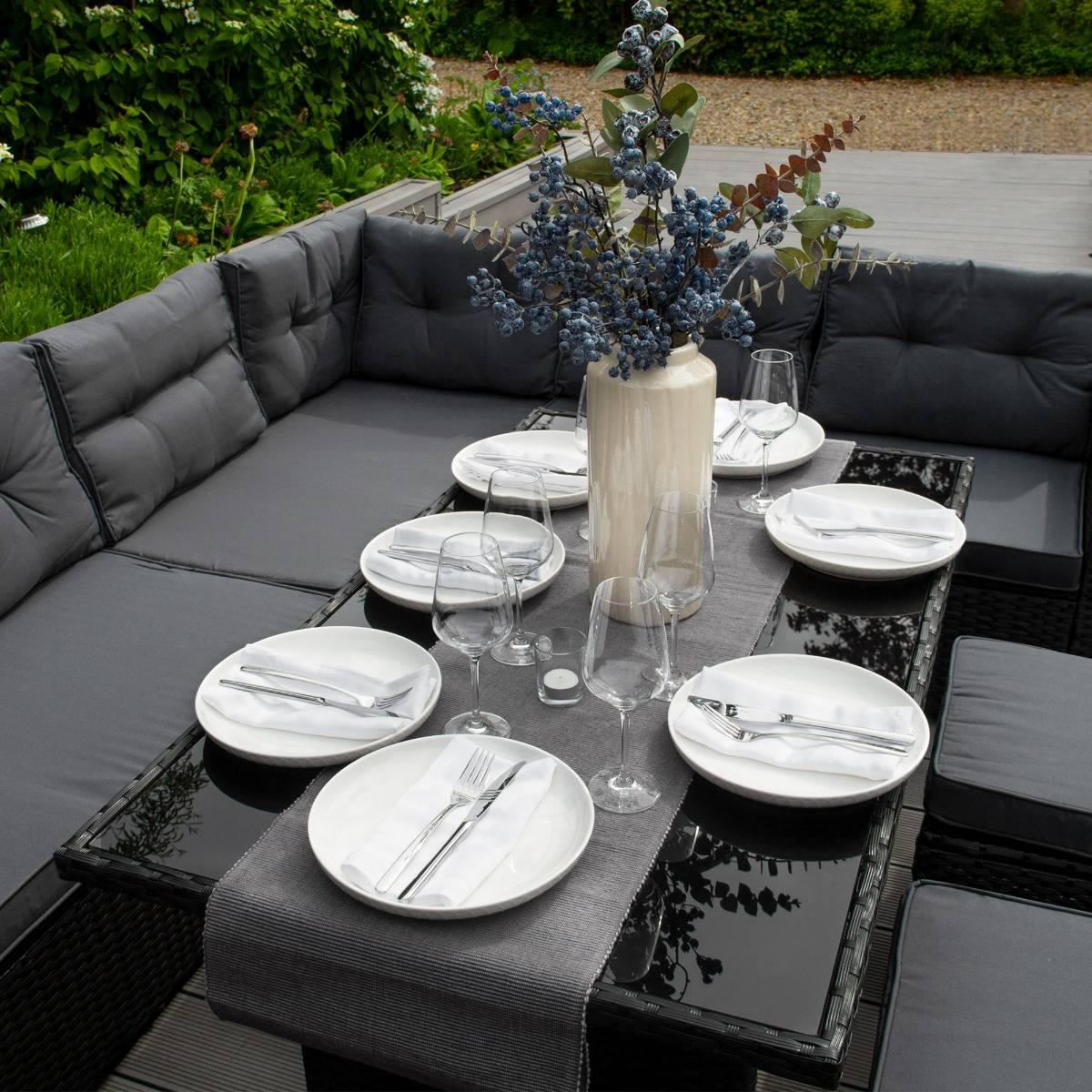 Mesa de comedor exterior con cojines oscuros y decoración de bayas azules.