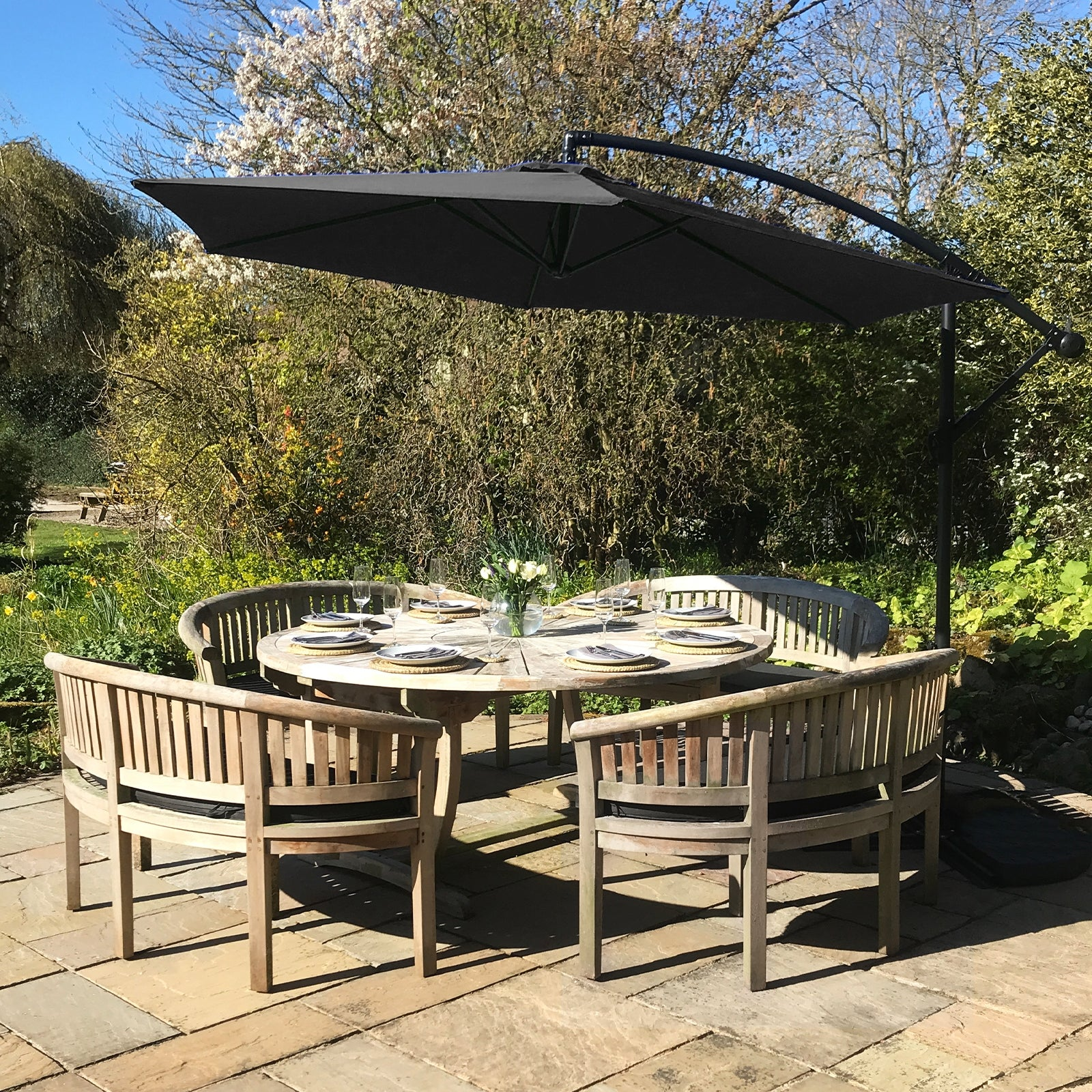 Conjunto de mesa y sillas de madera en un jardín, cubierto por un gran paraguas negro.
