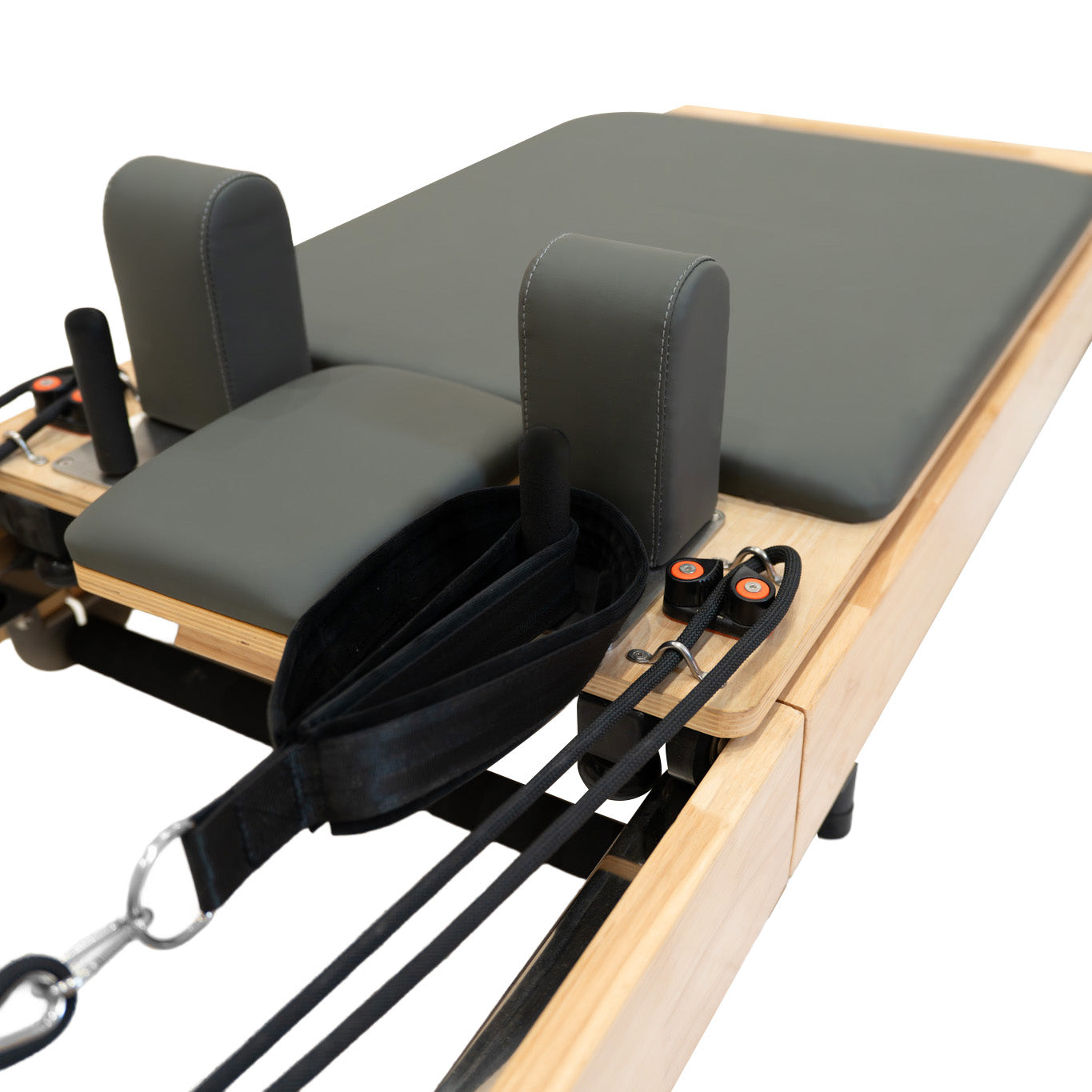 Un reformer de Pilates gris con marco de madera, correas y poleas sobre fondo blanco.