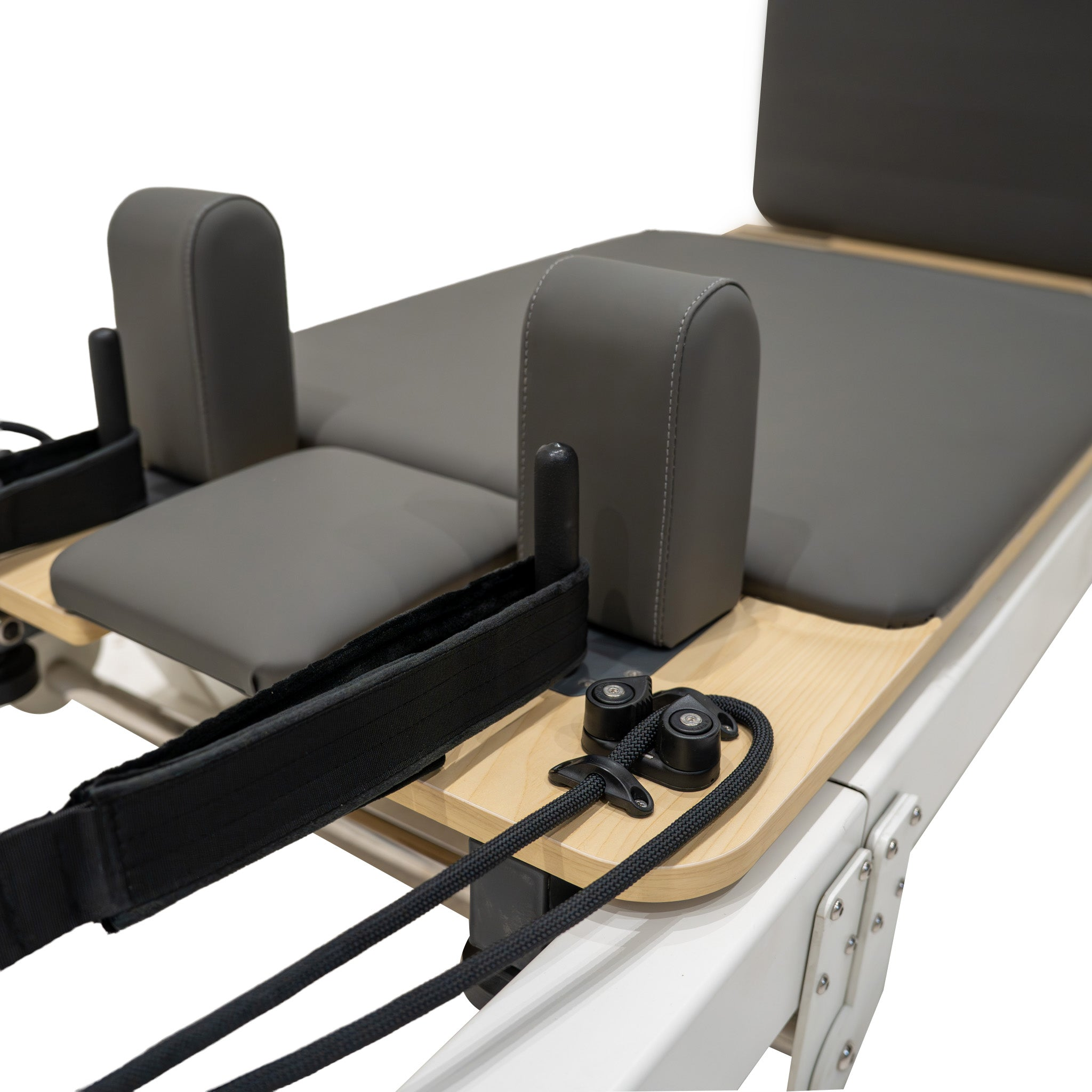 Un reformer de Pilates gris con correas y cuerdas negras sobre una plataforma de madera.