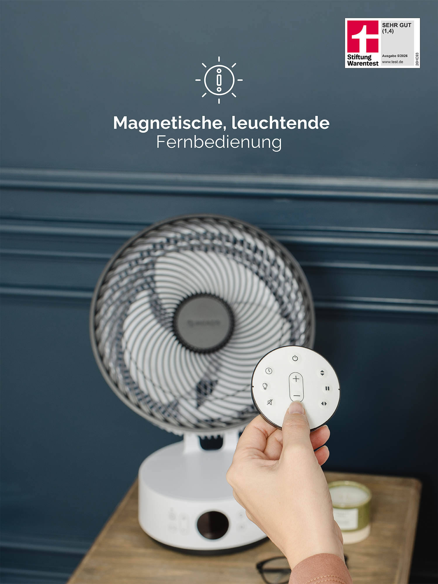 Eine Hand hält eine Fernbedienung mit Tasten neben einem weißen Ventilator. Text: 'Magnetische, leuchtende Fernbedienung'.