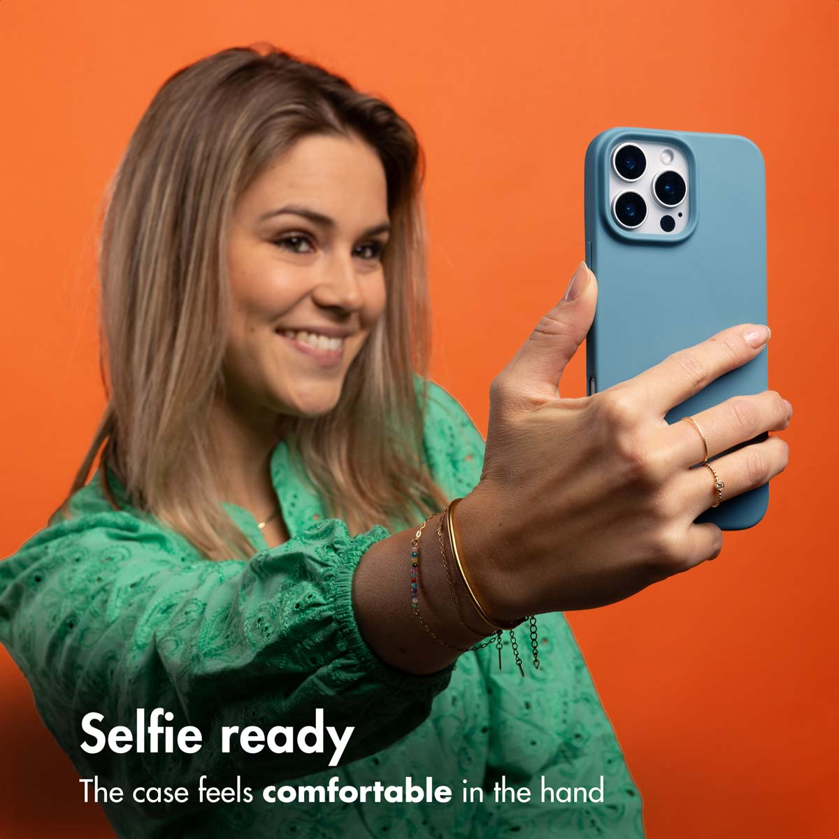 Kobieta w zielonej bluzce robi sobie selfie z niebieskim telefonem na pomarańczowym tle.