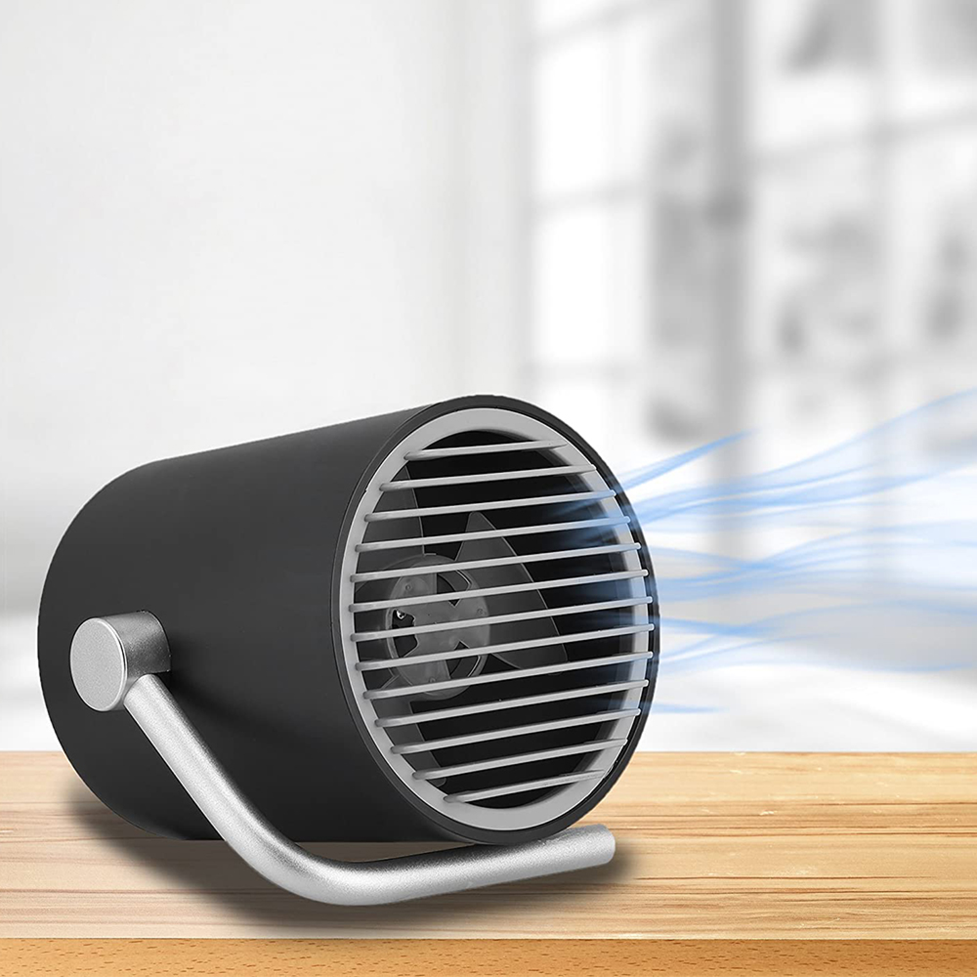 Ein schwarzer Tischventilator mit silbernem Griff auf einem Holztisch.