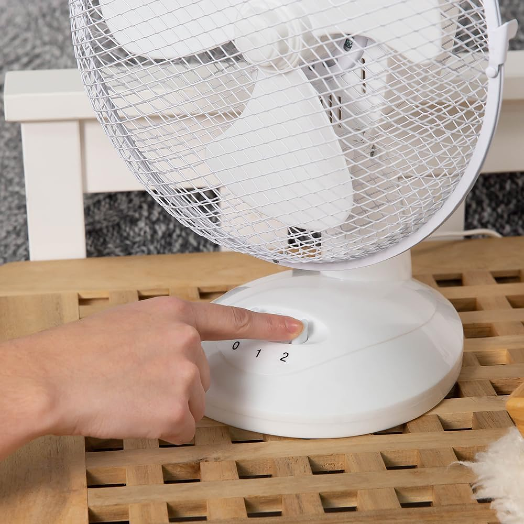 Eine Hand stellt einen weißen Ventilator auf Stufe 1 ein.