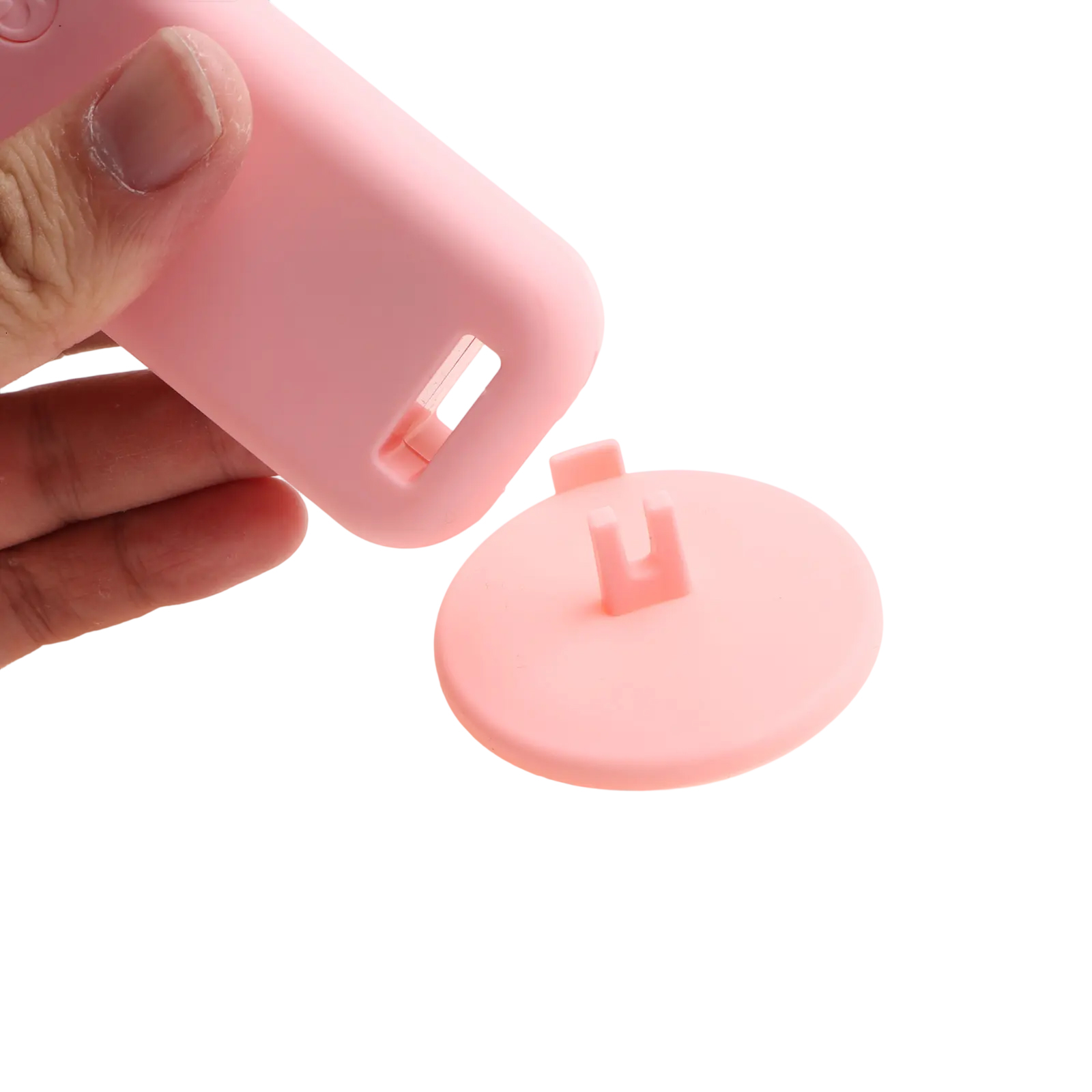 Eine Hand hält einen rosa Gegenstand. Eine runde Scheibe liegt daneben.