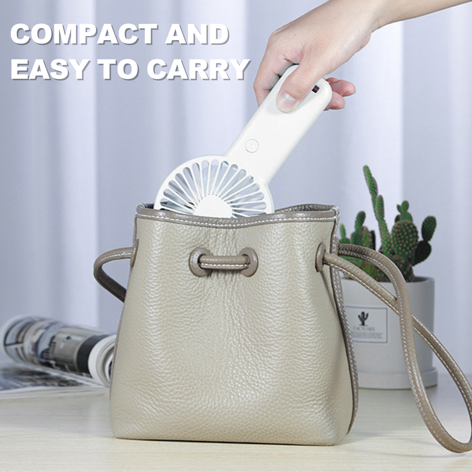 Eine Hand steckt einen weißen Ventilator in eine beige Tasche. Kaktuspflanze im Hintergrund.