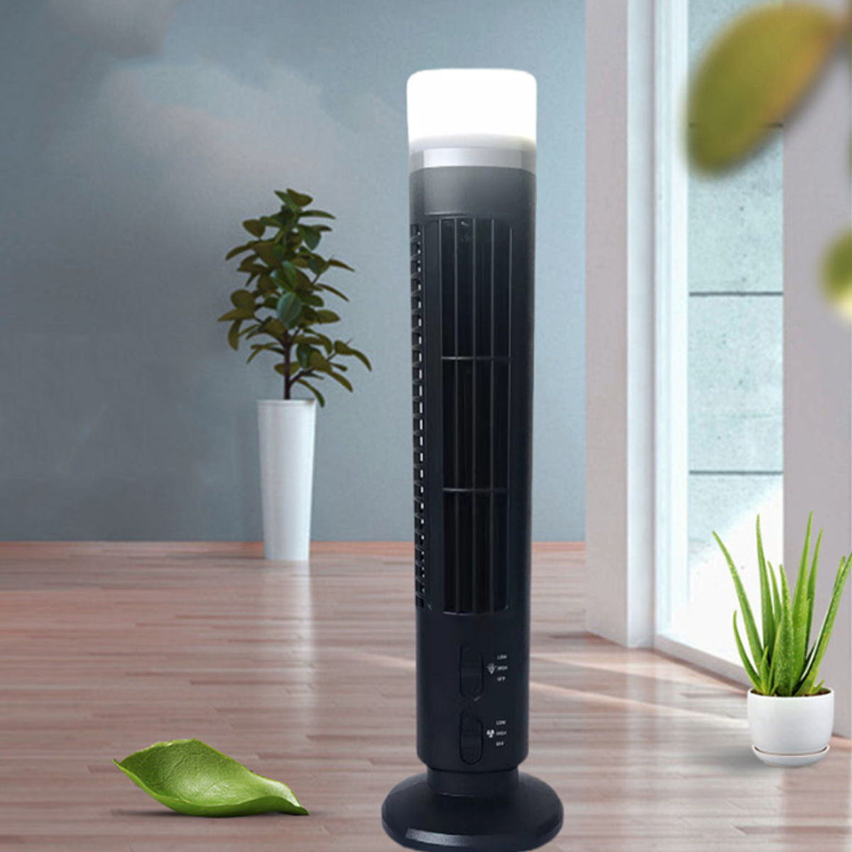 Ein schwarzer Turmventilator mit weißer Oberseite steht auf einem Holzboden. Pflanzen im Hintergrund.