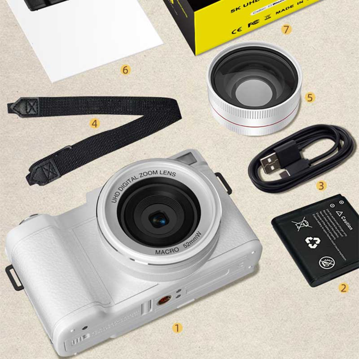 Eine weiße Digitalkamera mit Zubehör: Objektiv, Akku, Kabel, Tragegurt und Verpackung.