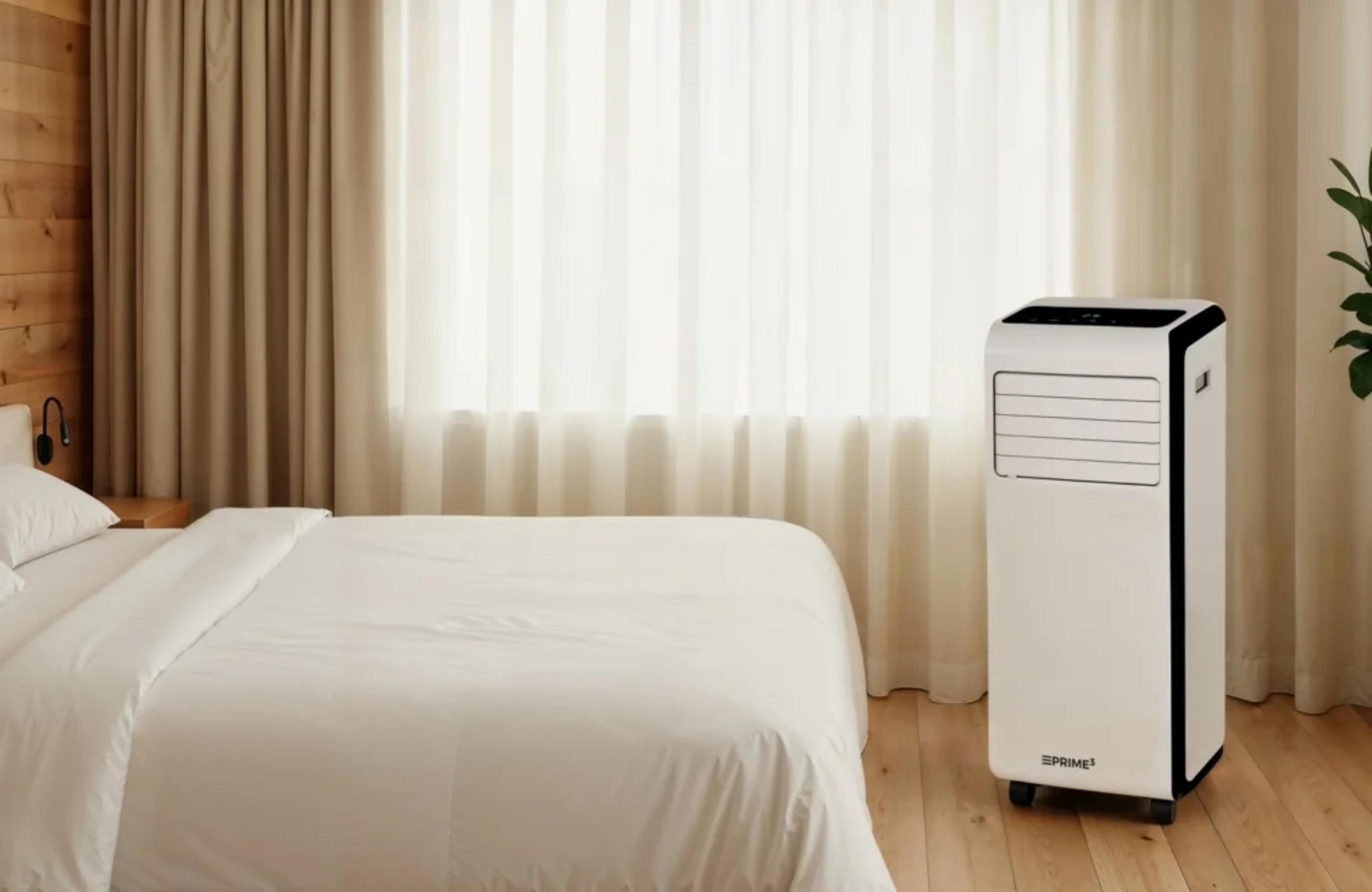 Una torre portatile per condizionatore bianco si trova accanto a un letto.