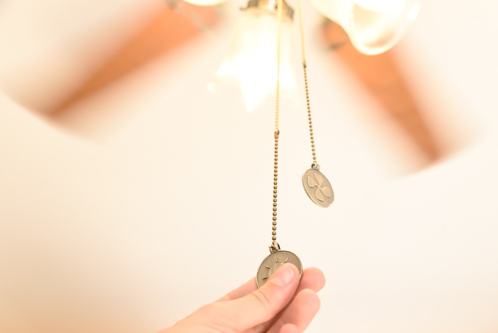 Eine Hand zieht an einer Kette mit einem Sonnensymbol für einen Deckenventilator.