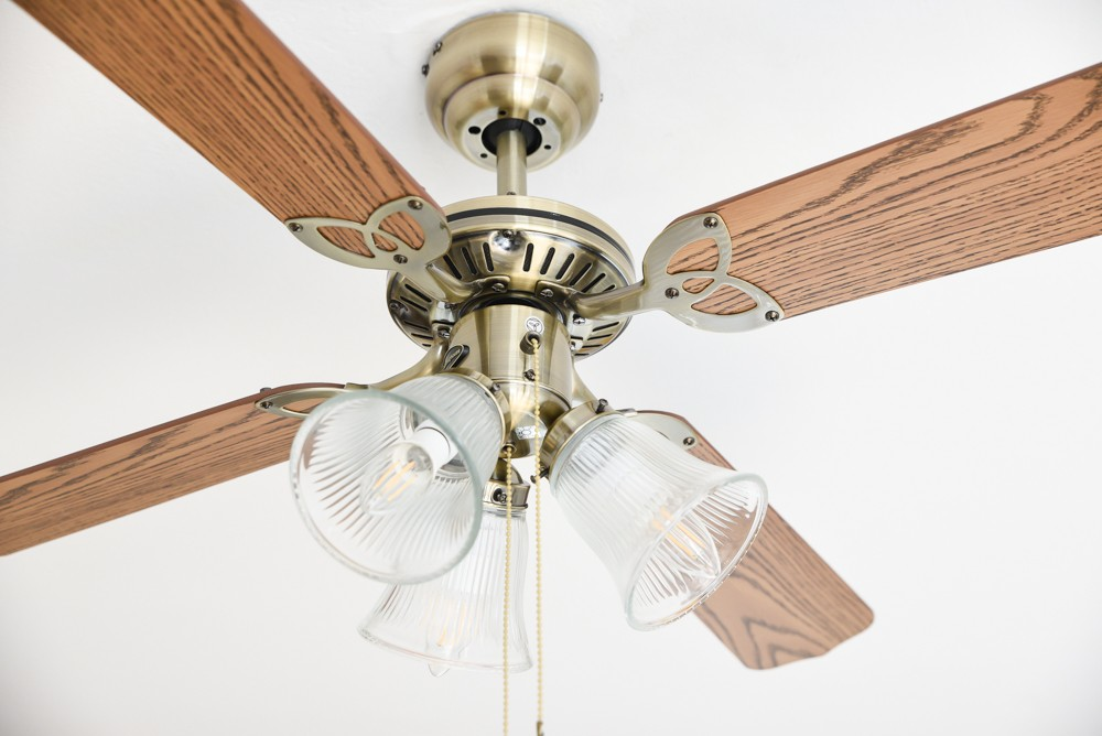 Deckenventilator mit Holzblättern und drei Glaslampenschirmen in Messingoptik.