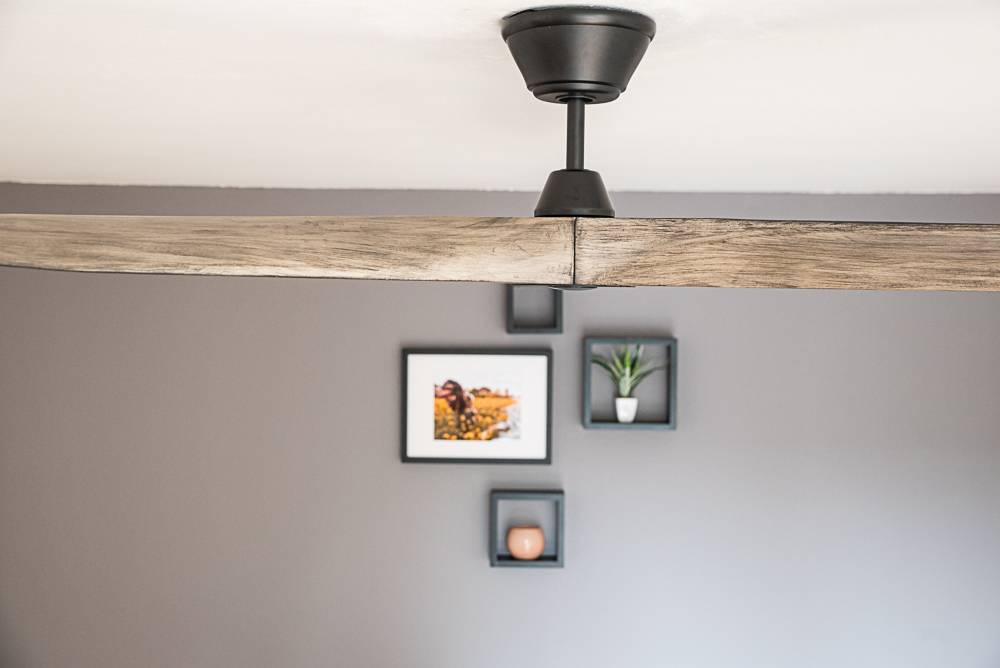 Un ventilatore a soffitto con pale effetto legno pende da un soffitto bianco.