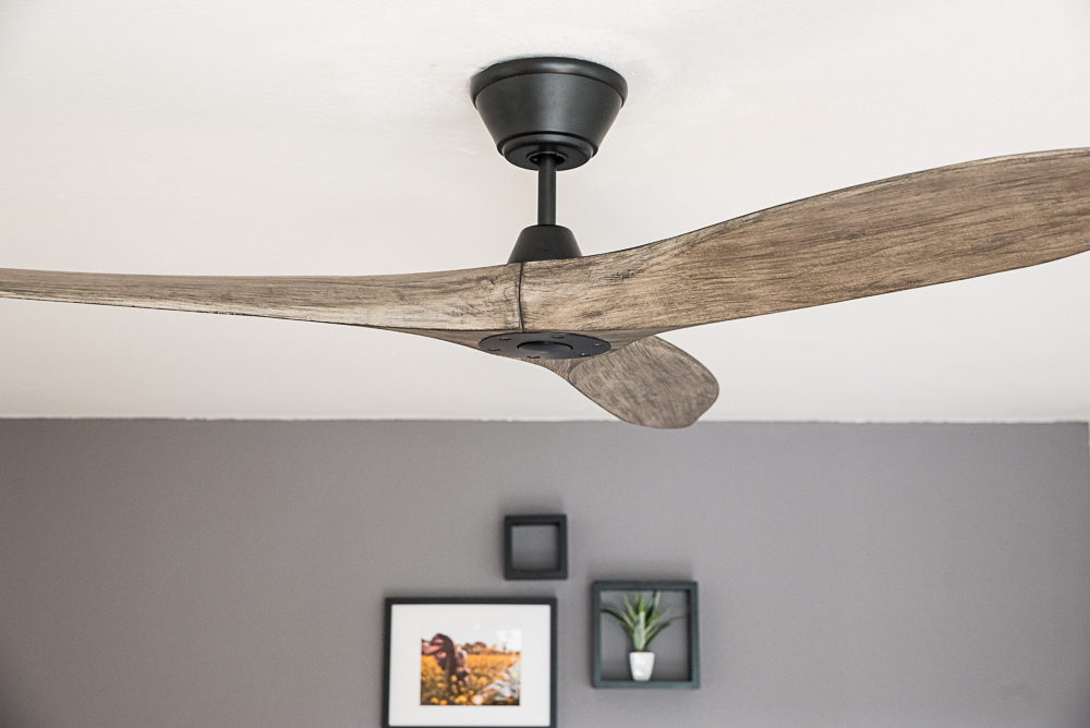 Un moderno ventilatore da soffitto con pale in legno pende da un soffitto bianco.