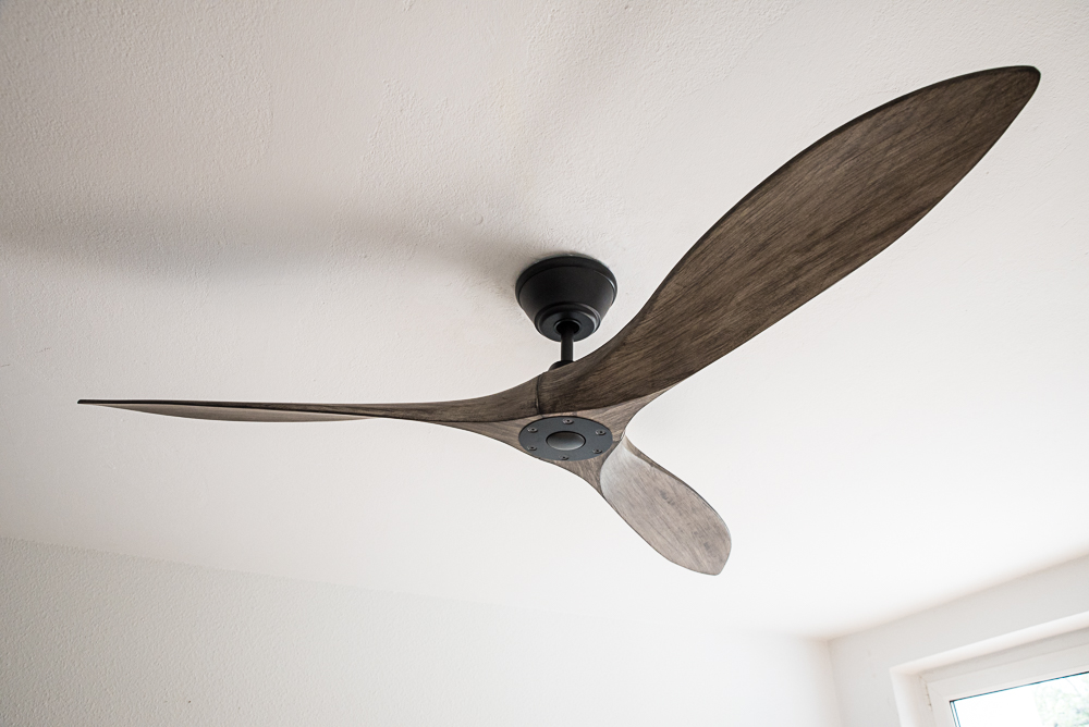 Un ventilatore da soffitto moderno con tre pale in legno e alloggiamento motore nero.
