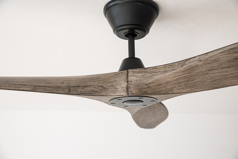 Un moderno ventilatore da soffitto con corpo in metallo scuro e pale in legno.