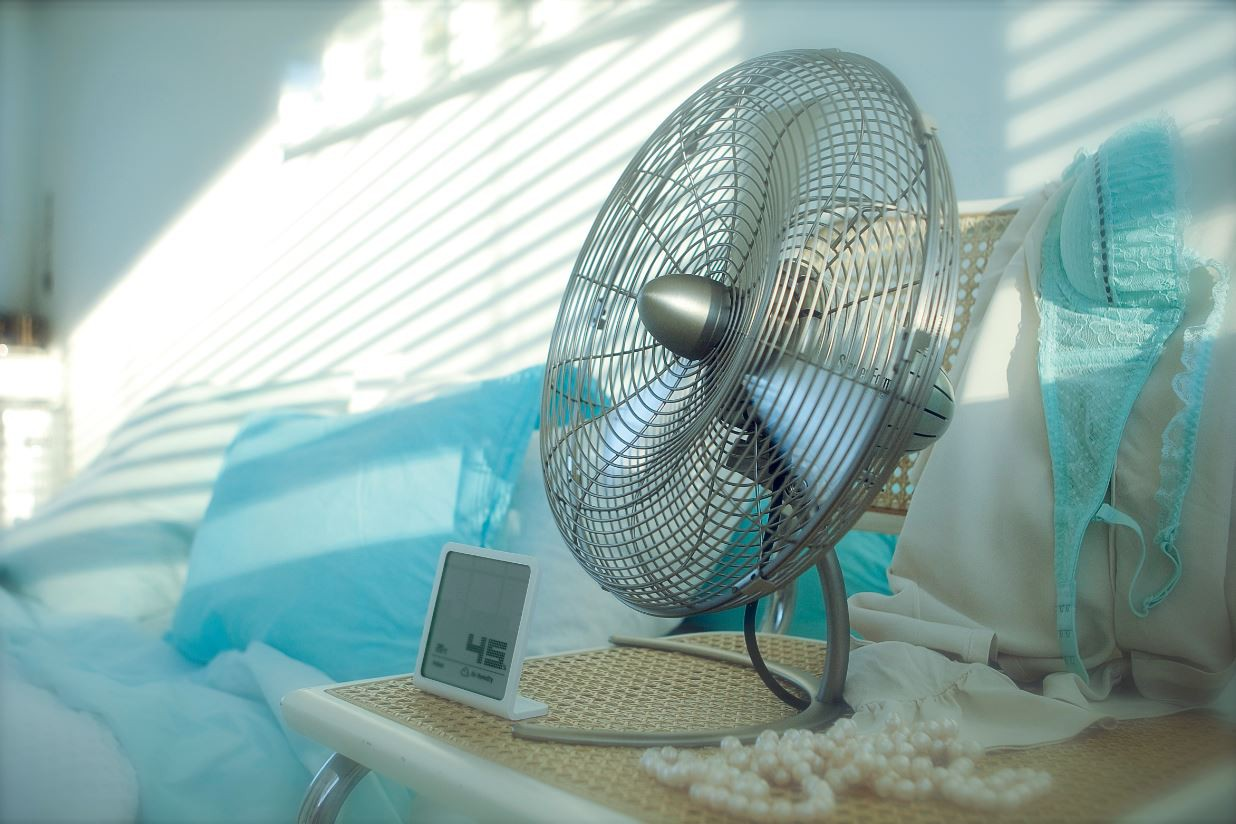 Un ventilateur en métal est posé sur une table à côté d'un thermomètre numérique et d'un soutien-gorge turquoise.