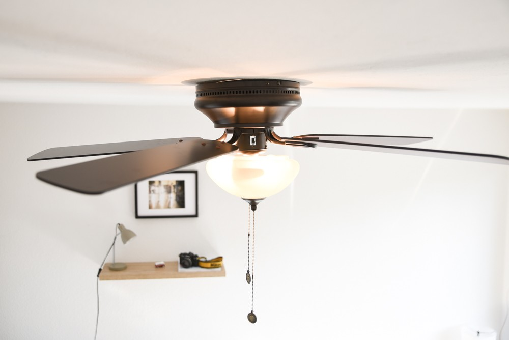 Deckenventilator mit Licht, darunter ein Regal mit Lampe und Kamera.