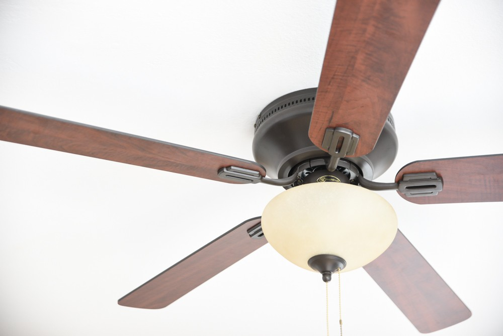 Eine Deckenventilator mit vier Holzflügeln und einer Milchglaskuppel.