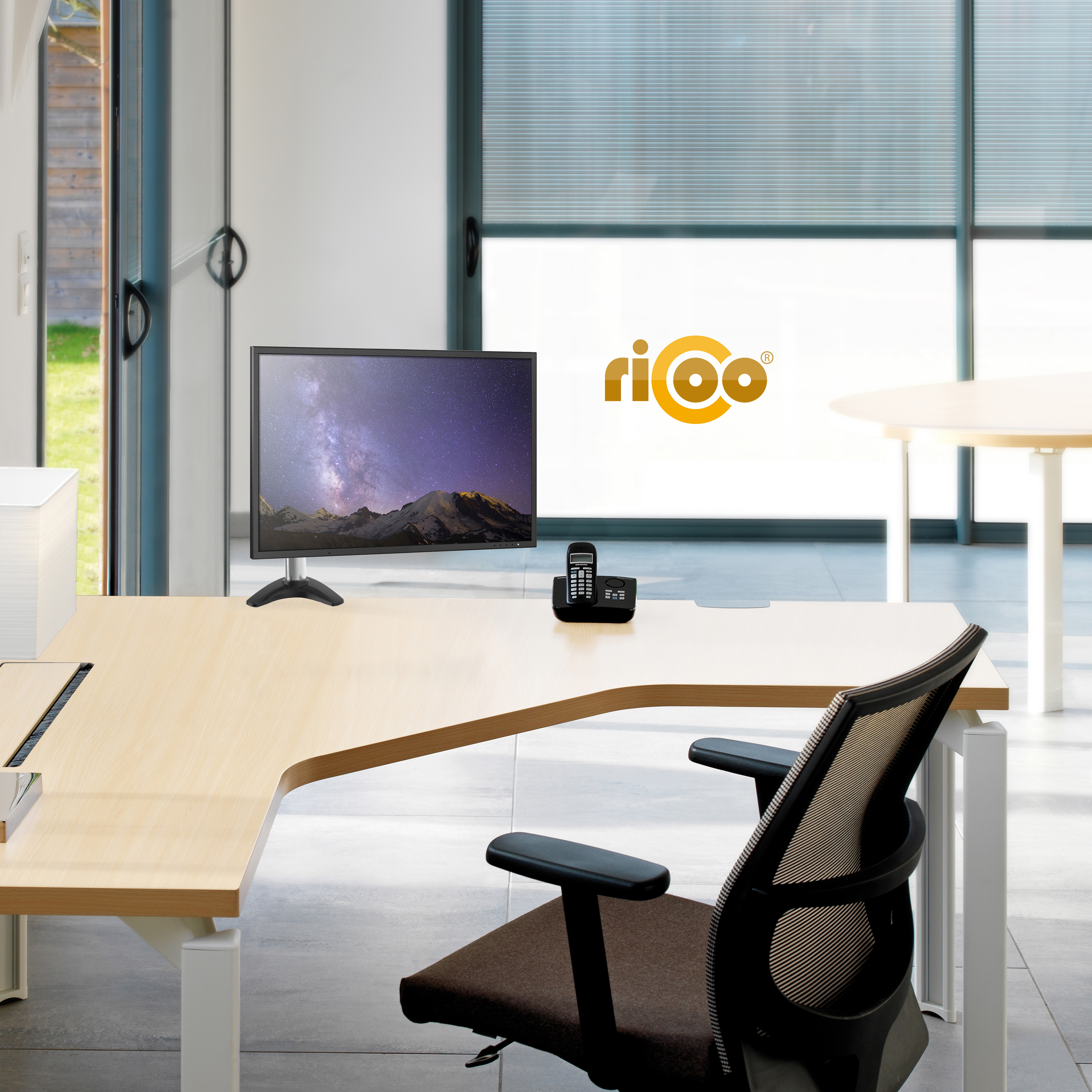 Ein modernes Büro mit einem hellen Holztisch, schwarzem Stuhl und Computermonitor.