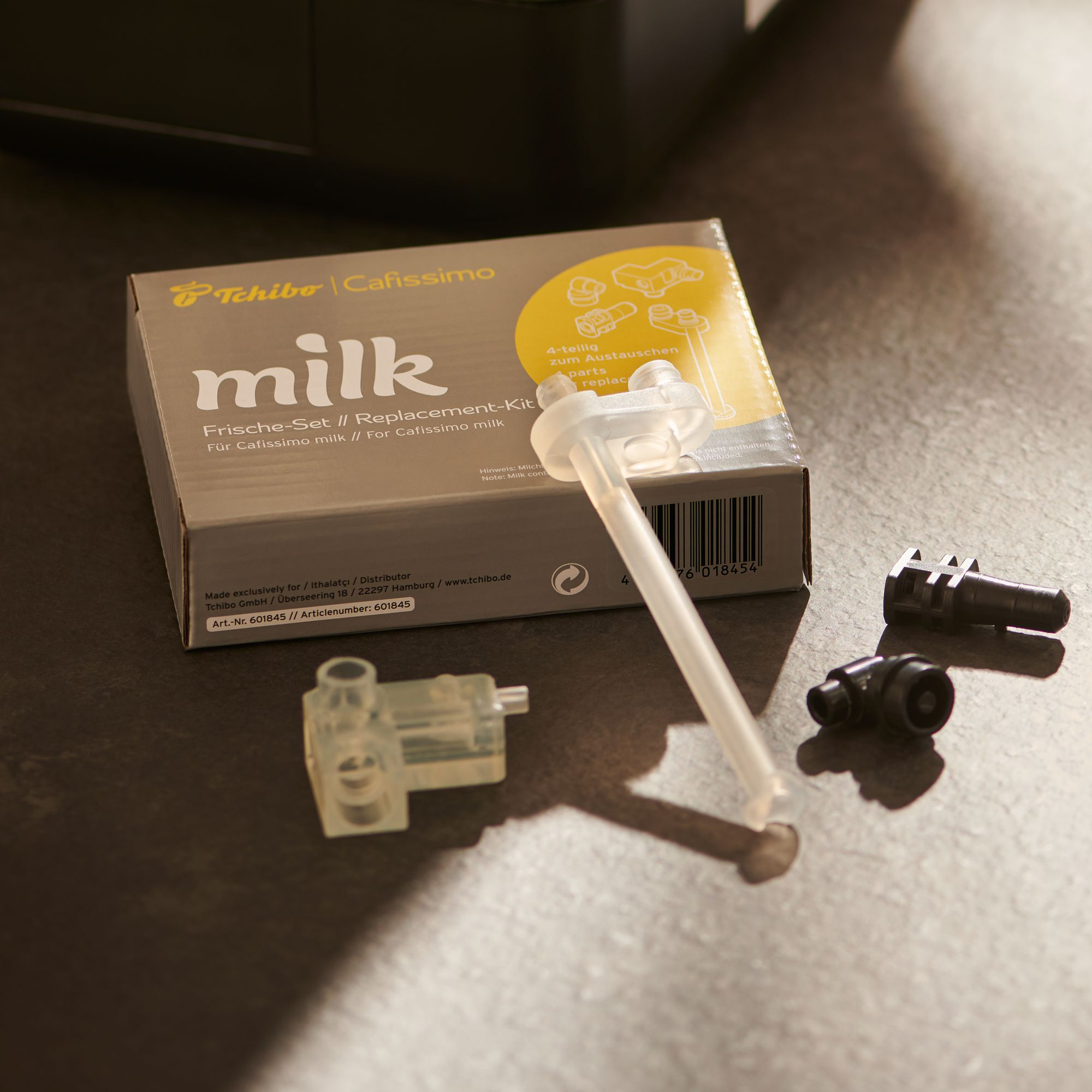 Tchibo Cafissimo Milch Ersatzteile auf grauem Untergrund.