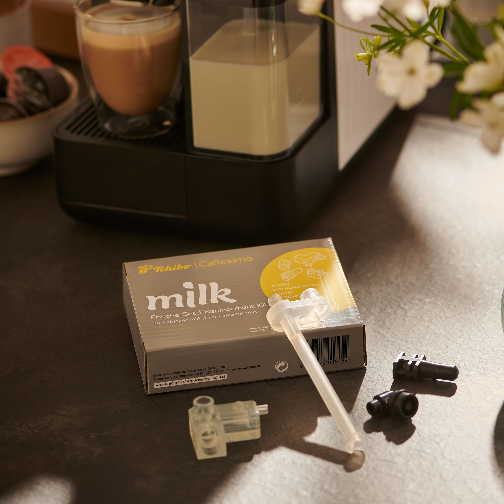 Ein Tchibo Cafissimo Milch-Ersatzteil-Set liegt auf einem Tisch.