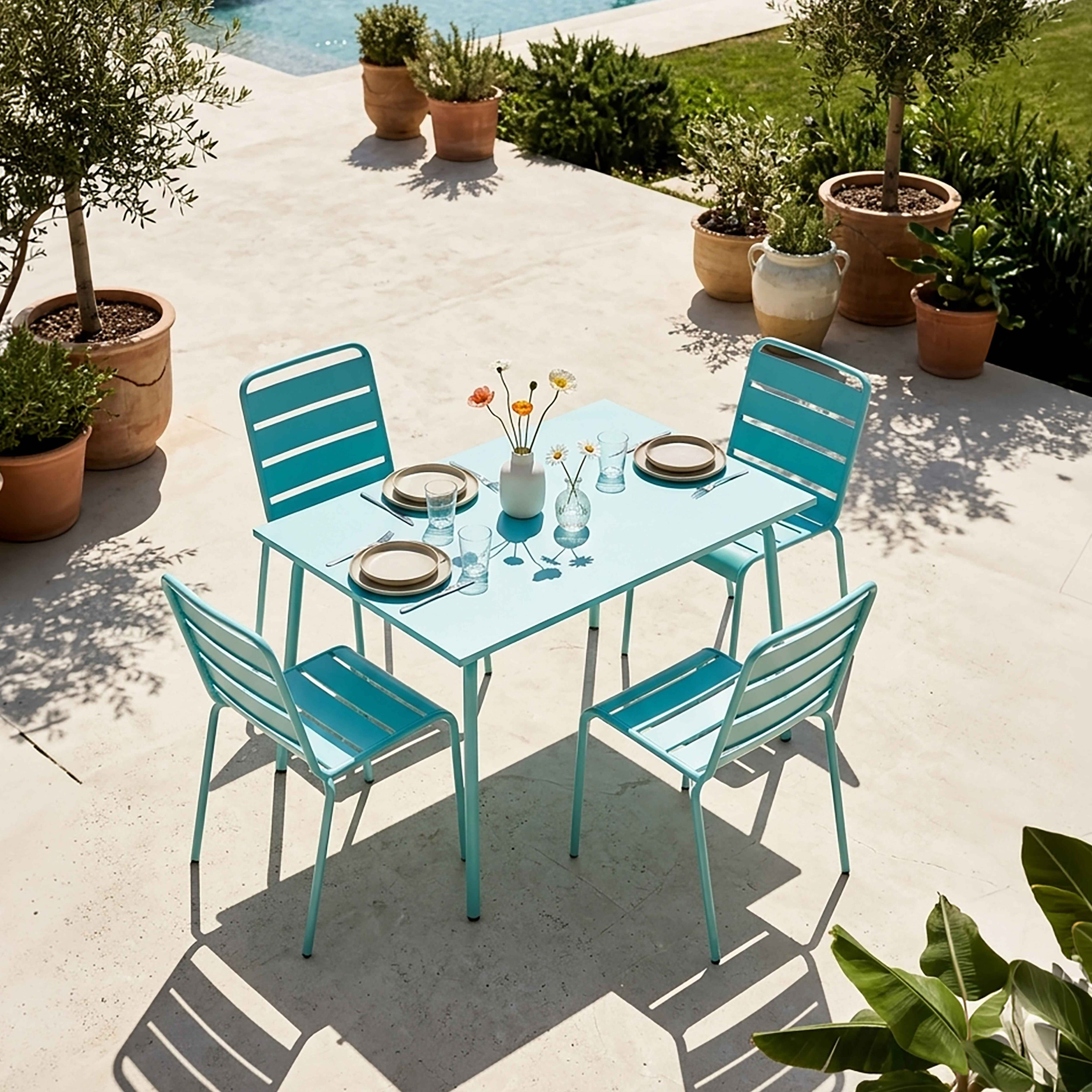Ein hellblauer Tisch mit Stühlen ist für ein Essen im Freien neben einem Pool gedeckt.