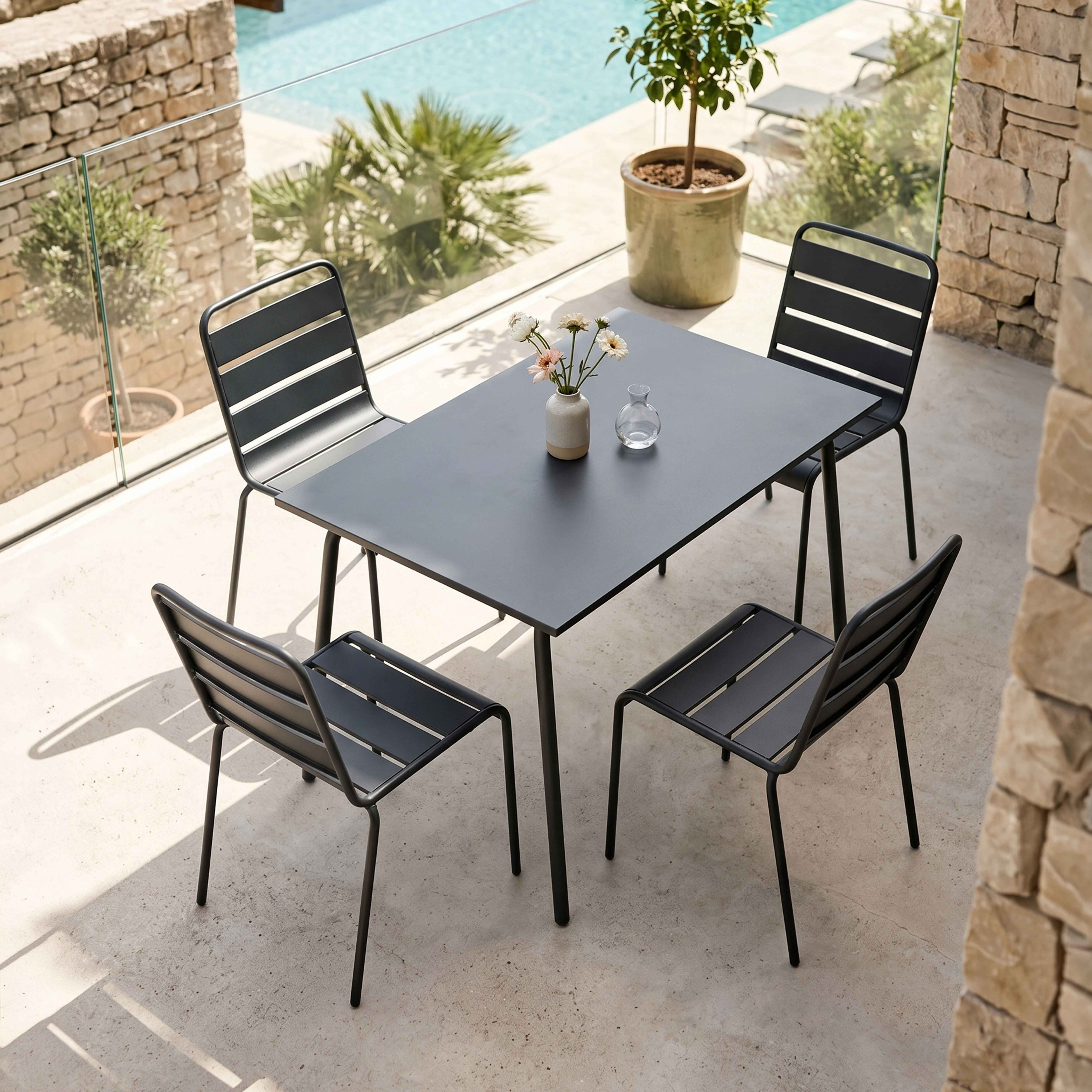 Schwarzer Tisch mit vier Stühlen auf einer Terrasse, mit Pool im Hintergrund.
