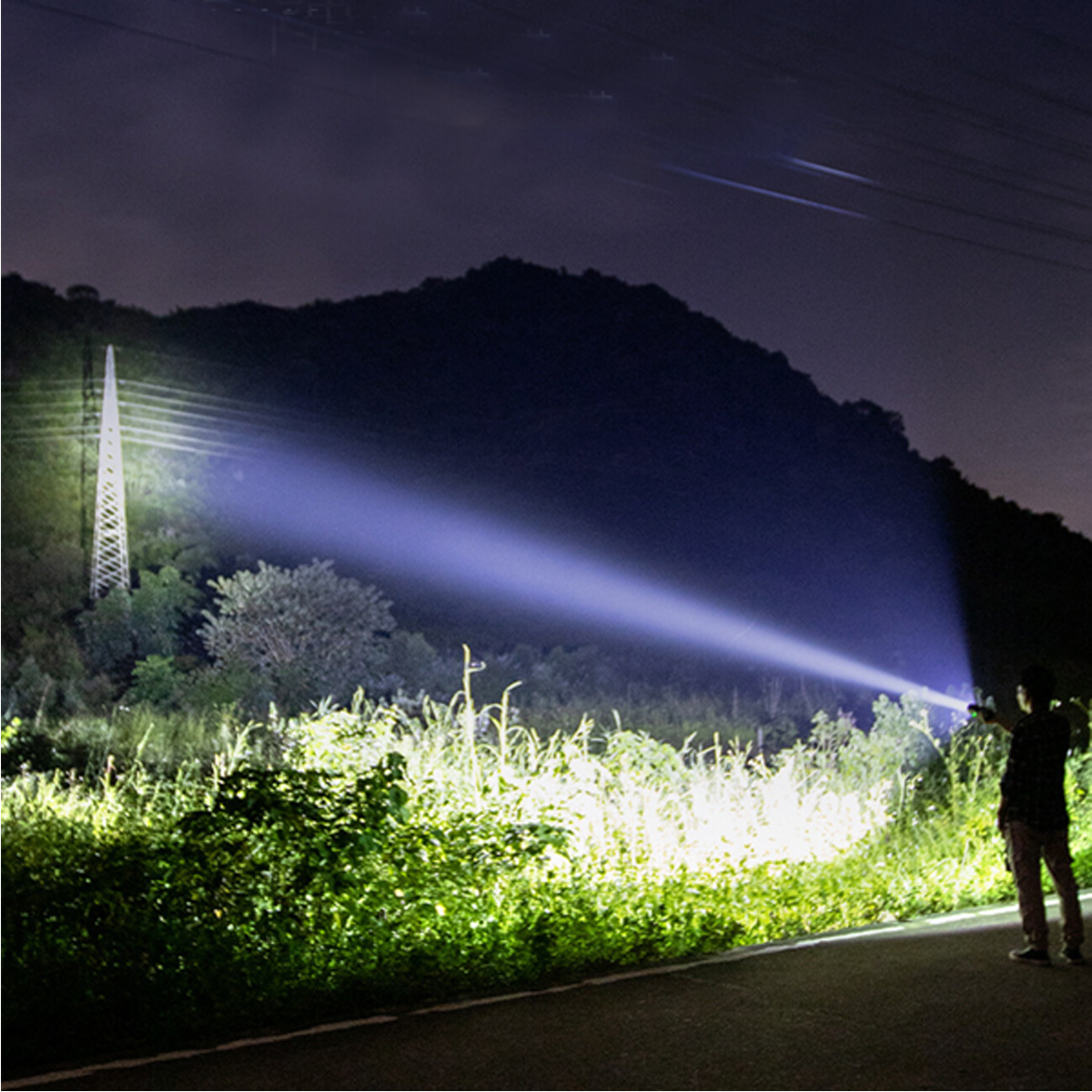 Mann leuchtet mit Taschenlampe auf Feld und Berg bei Nacht.
