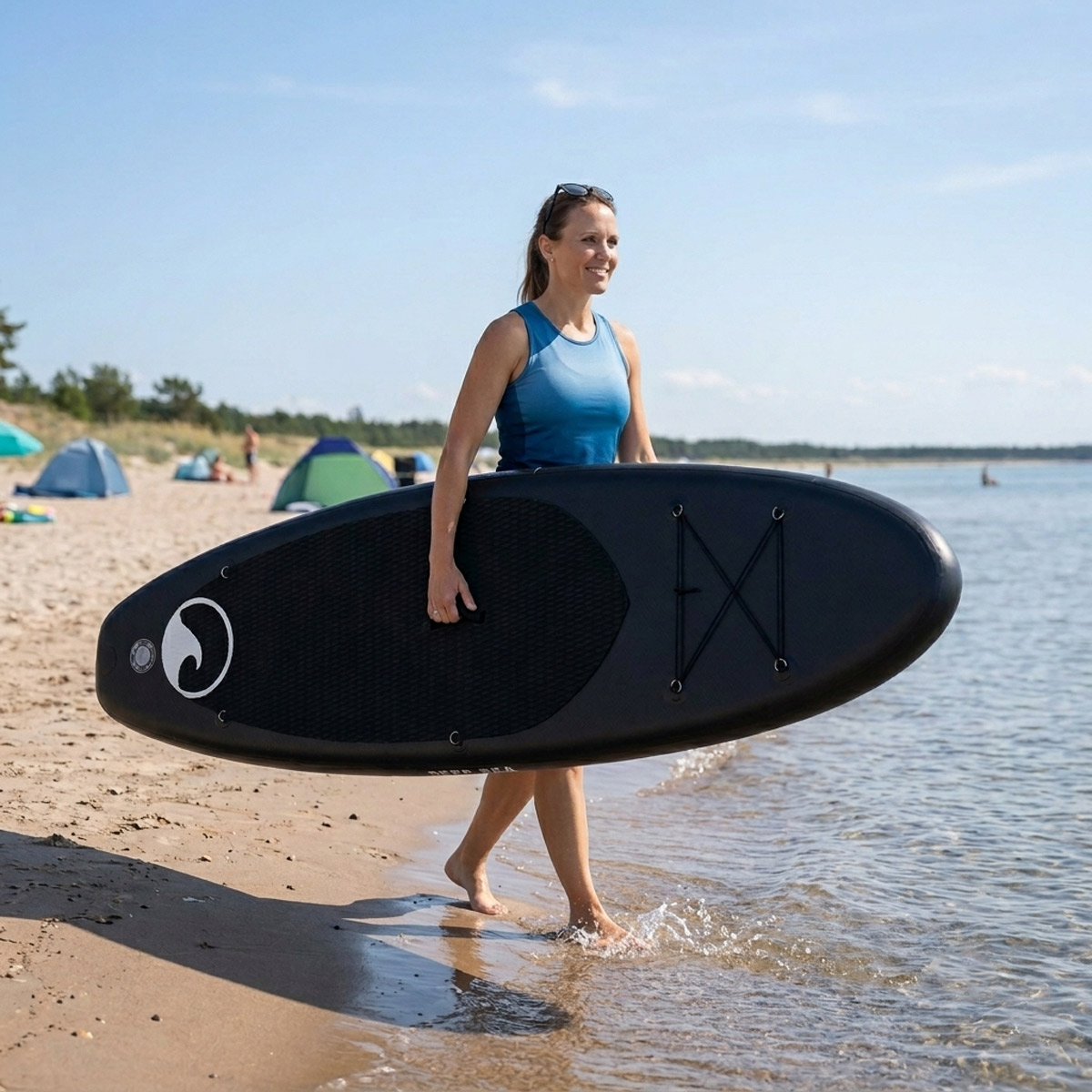 Kobieta niesie czarną deskę SUP do wody na plaży.