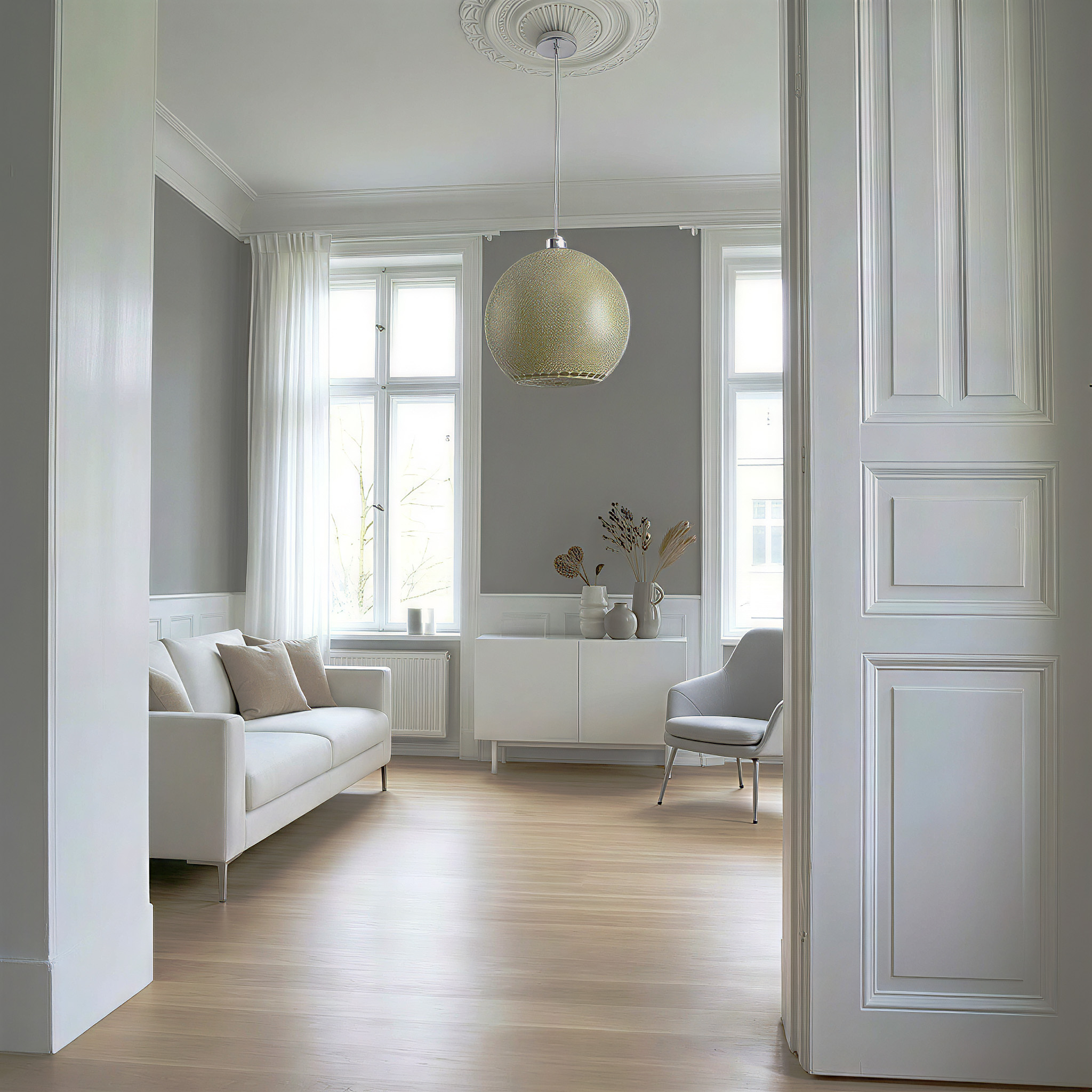 Ein helles Wohnzimmer mit Sofa, Schrank, Sessel und Fenstern.