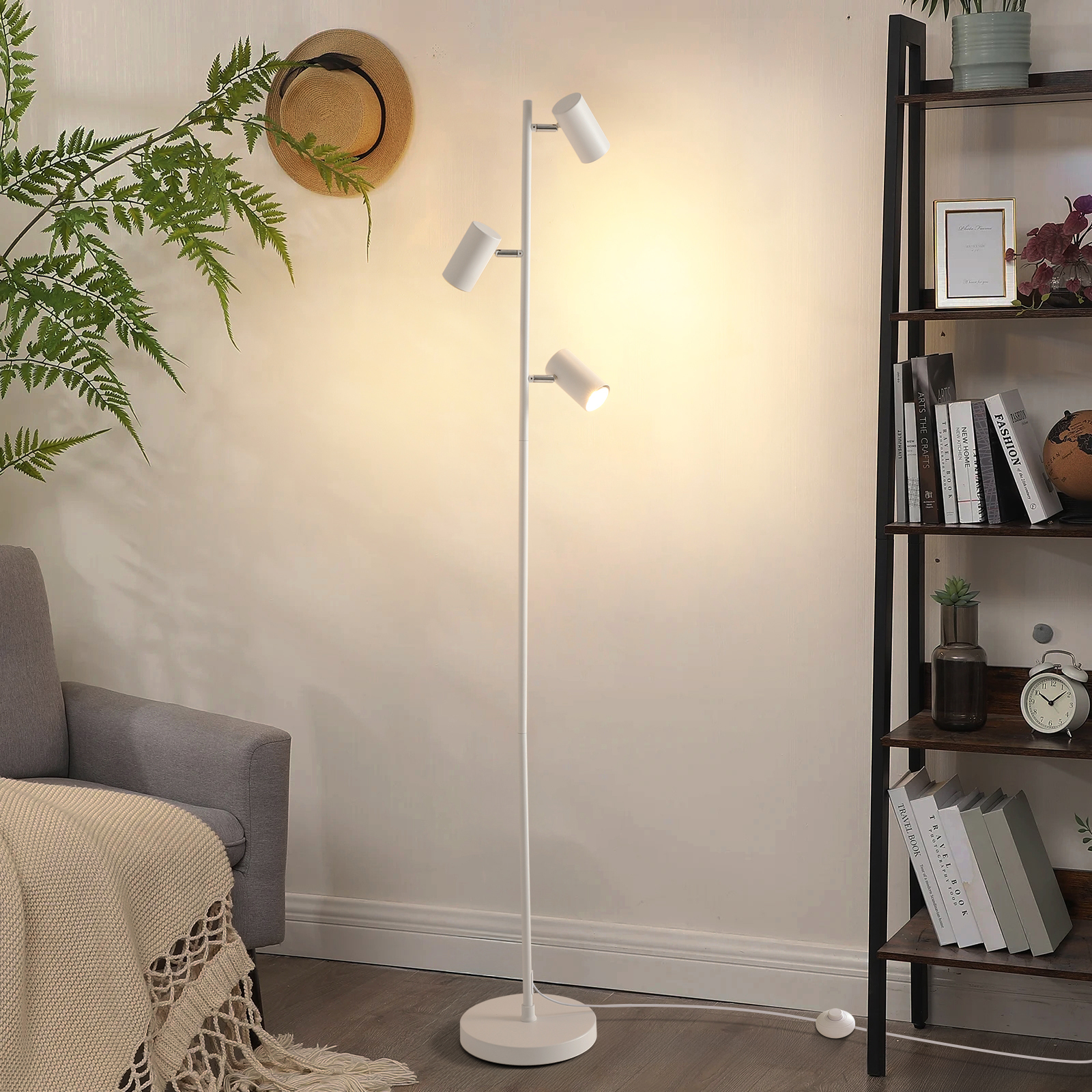 Ein weißer Stehlampen-Spot mit drei Lichtern steht neben einem Sessel.