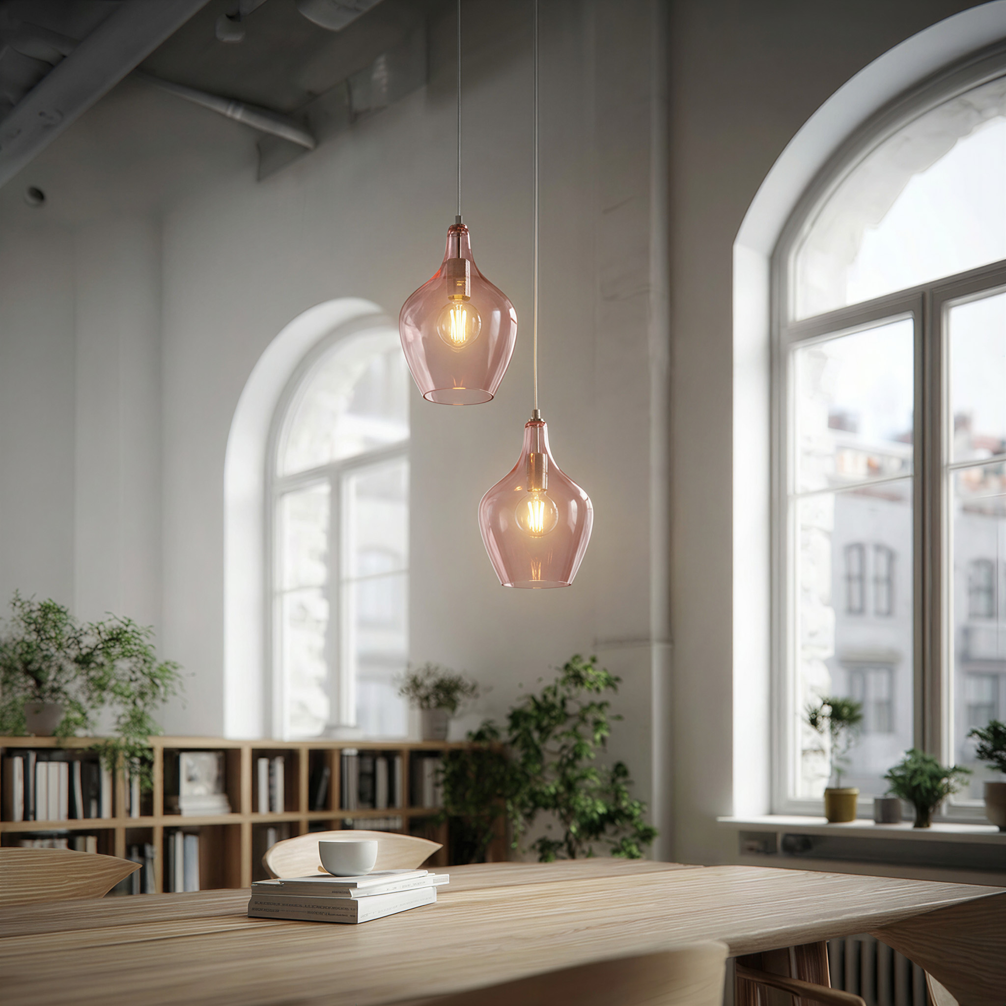 Zwei rosafarbene Glaspendelleuchten hängen über einem Holztisch mit Büchern und einer Schale.