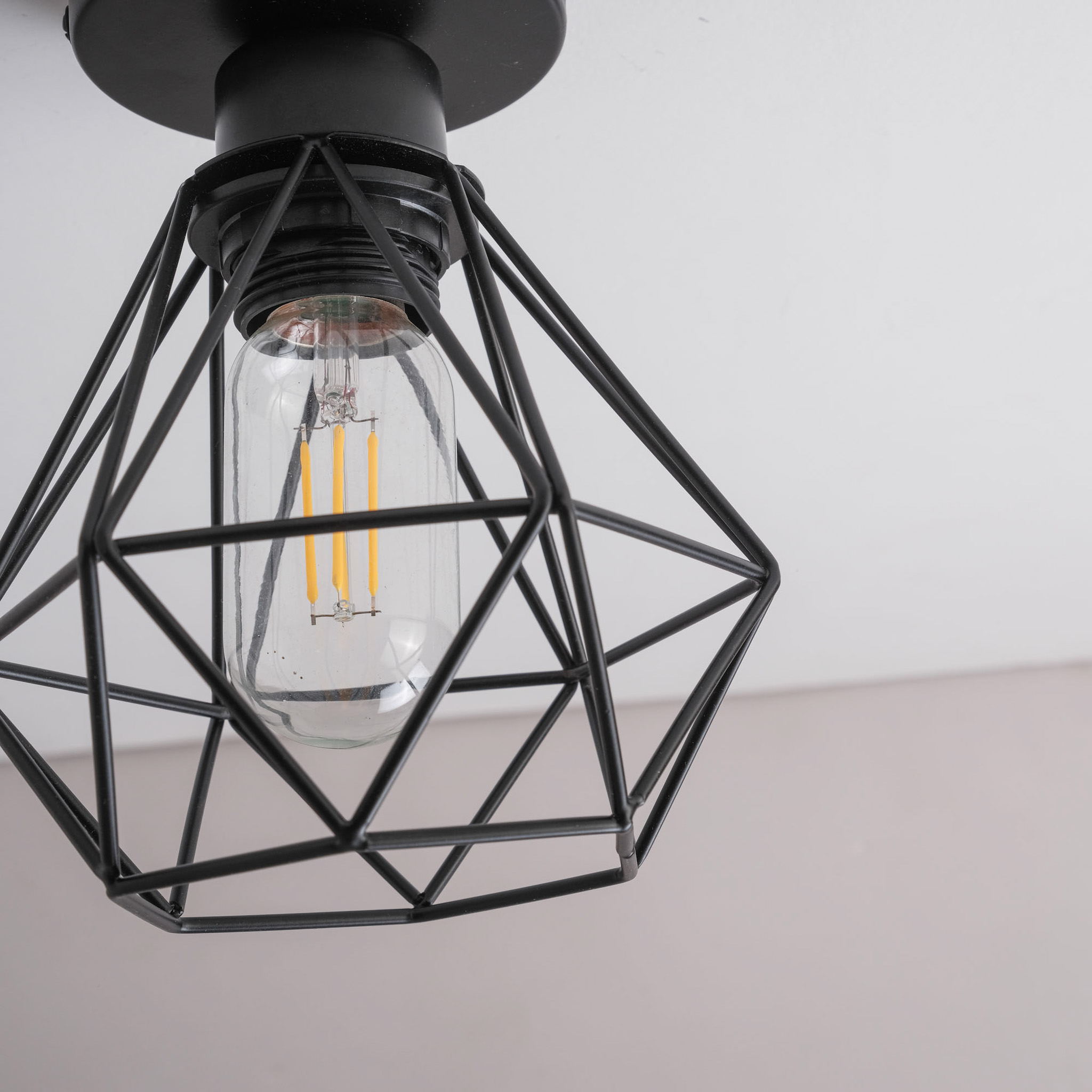 Eine schwarze Lampe mit einem geometrischen Käfig und einer Edison-Glühbirne.