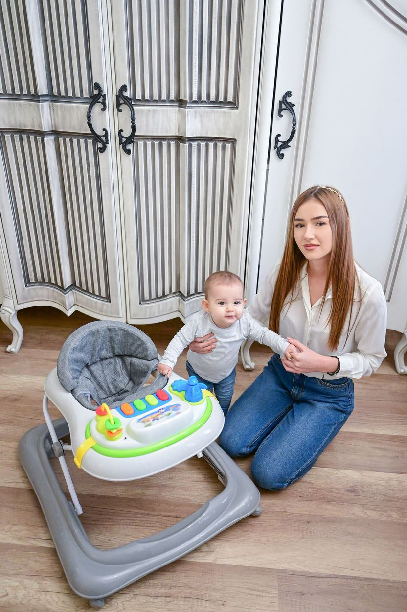 Eine Frau kniet neben einem Baby in einem Gehfrei vor einem Schrank.