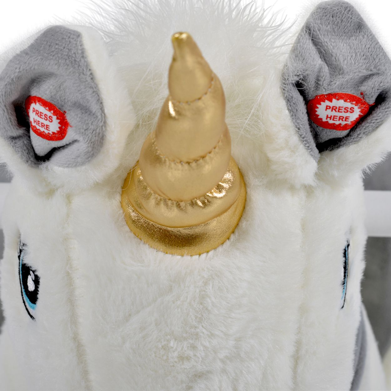 Ein weißes Plüsch-Einhorn mit goldenem Horn und grauen Ohren mit roten Aufklebern.