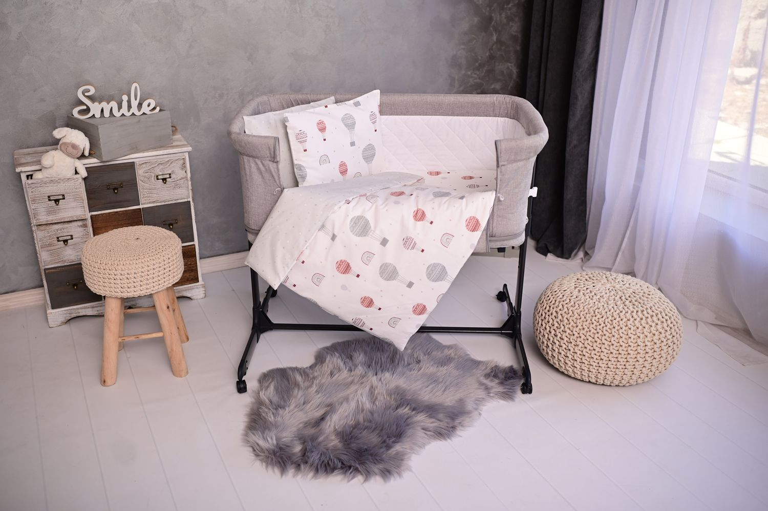 Ein Babybett mit Heißluftballon-Bettwäsche, einem Hocker und einem Teppich.