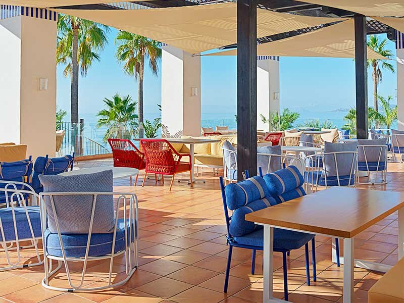 Un patio cubierto con muebles azules y blancos con vistas al mar.