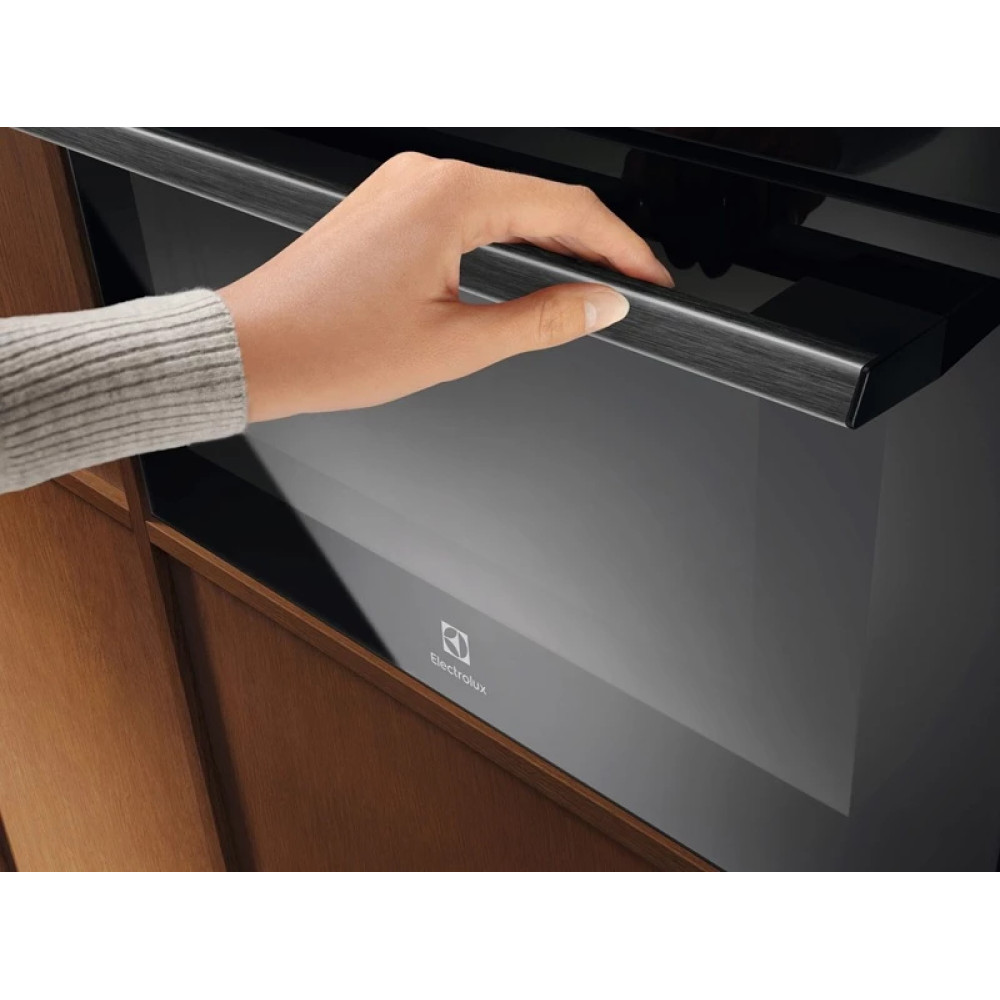 Ręka otwiera nowoczesny czarny piekarnik Electrolux z srebrną rączką.