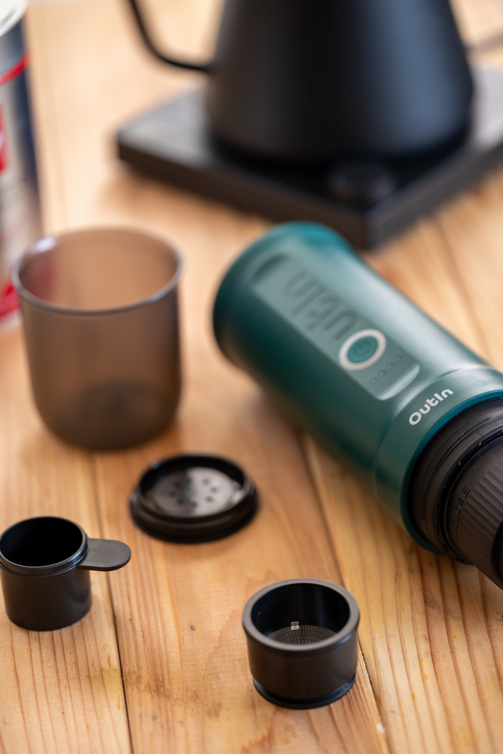 Cafetera portátil Outlin verde en mesa de madera con accesorios.