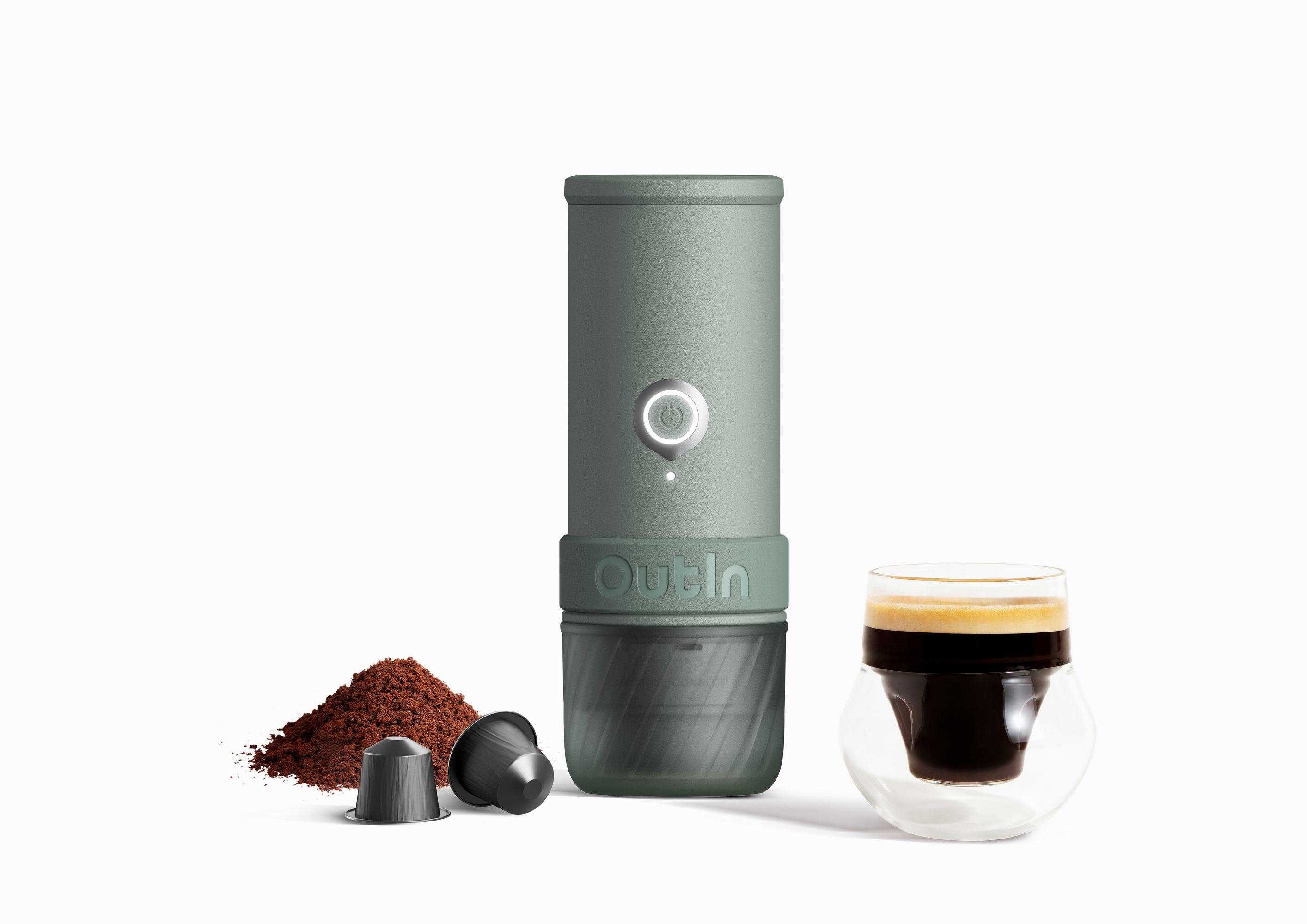 Una cafetera verde con posos de café, cápsulas y un vaso de espresso.