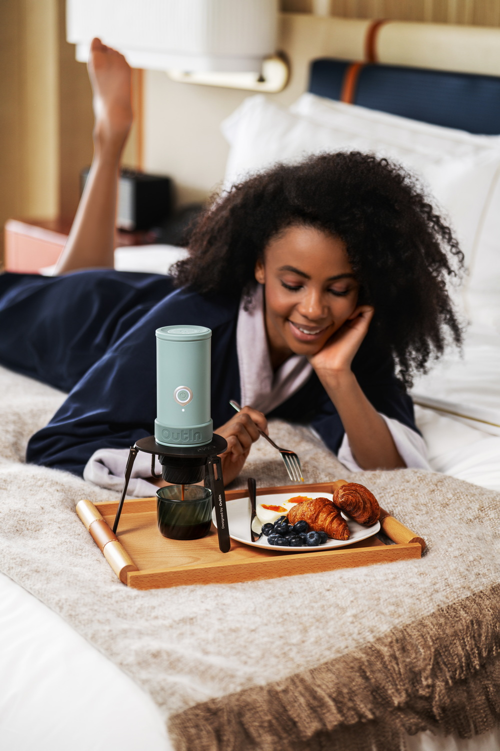 Una mujer yace en la cama disfrutando del desayuno con café y cruasanes.