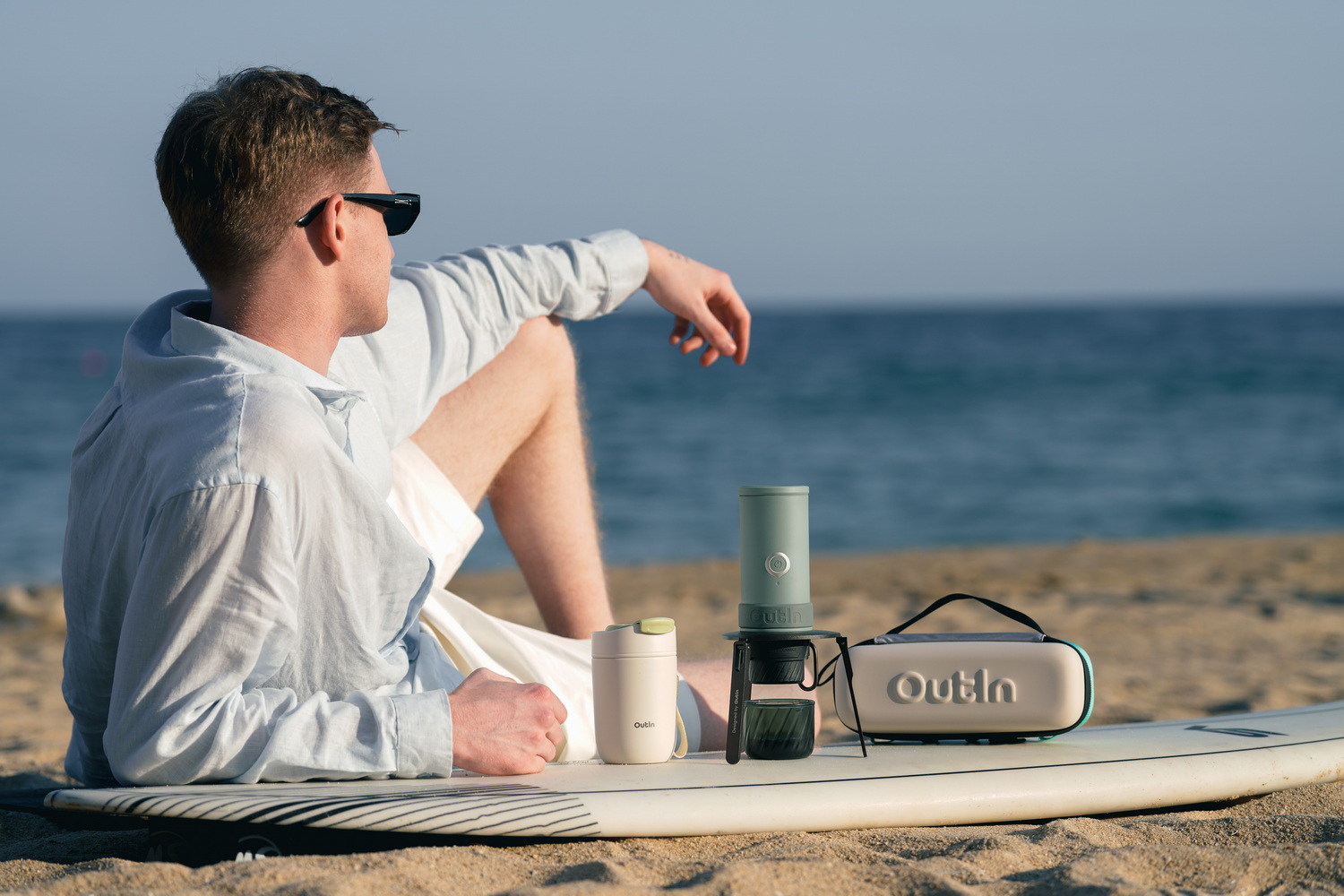 Hombre en tabla de surf junto al mar con cafetera y taza.