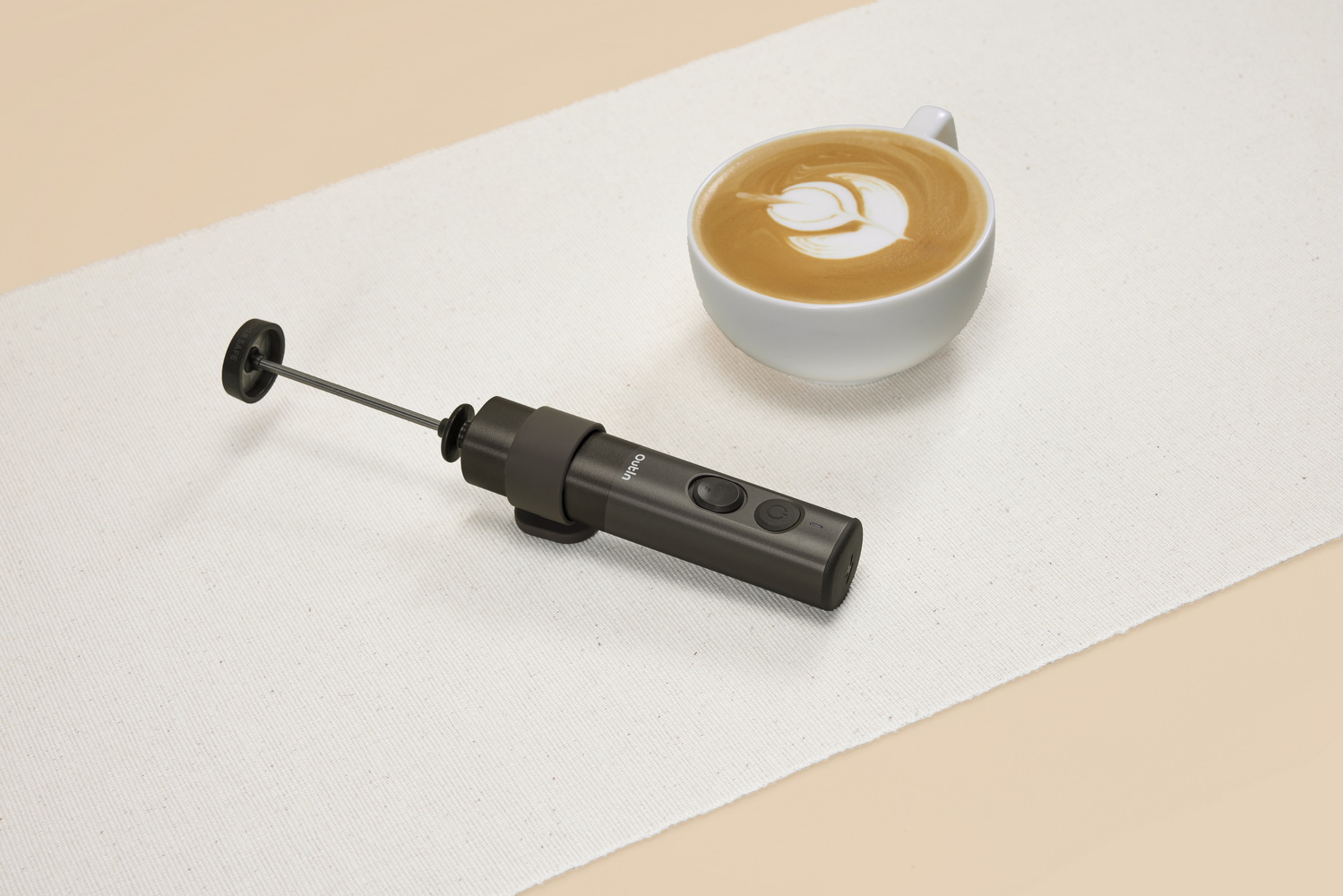 Un espumador de leche oscuro yace junto a una taza de café con latte art.