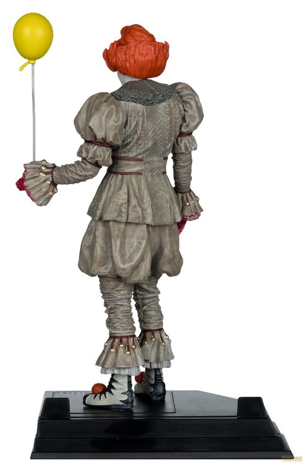 Eine Clownfigur mit orangefarbenem Haar hält einen gelben Ballon. Sie trägt ein graues Kostüm.