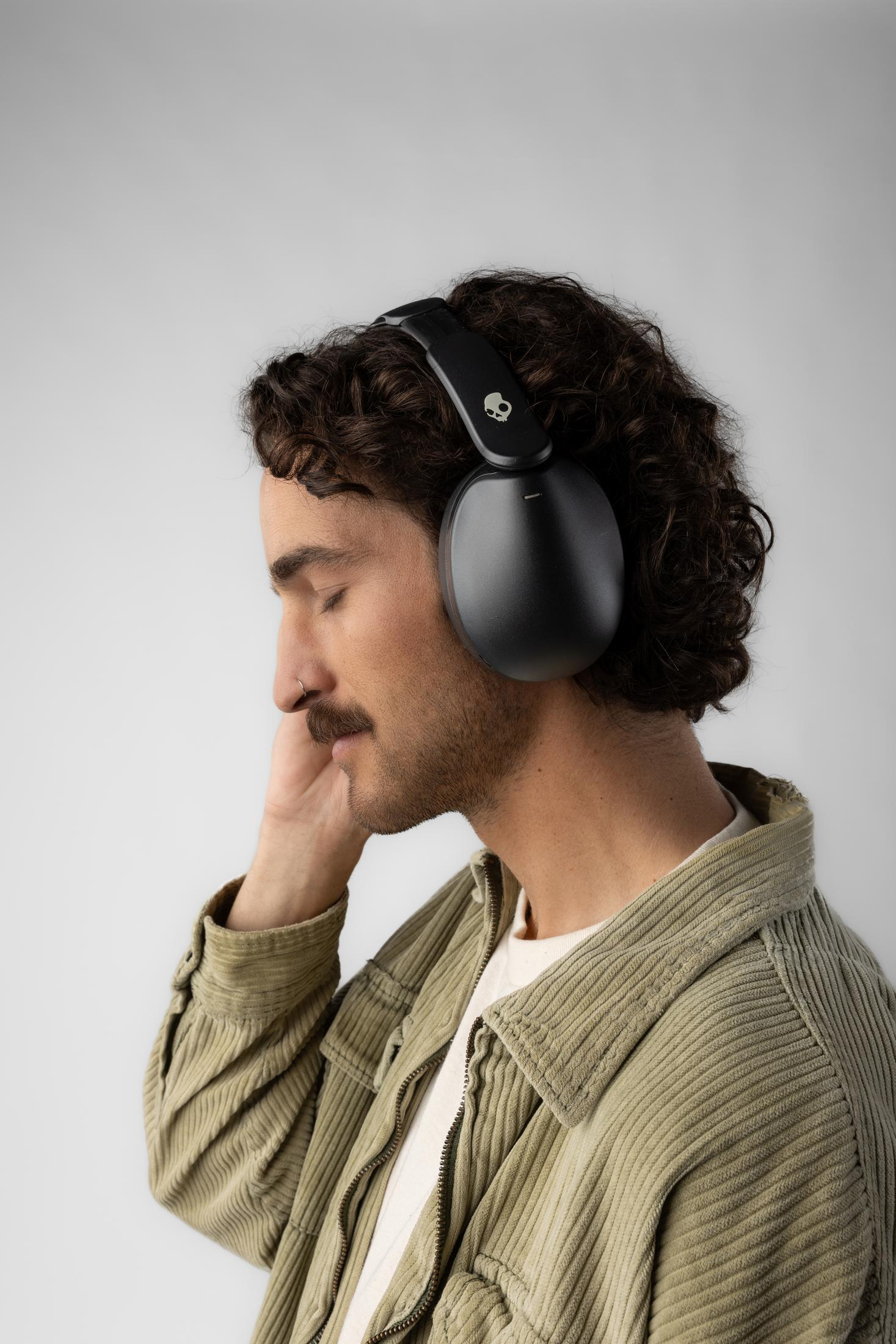 Un uomo con capelli ricci e baffi indossa cuffie, ascoltando musica.