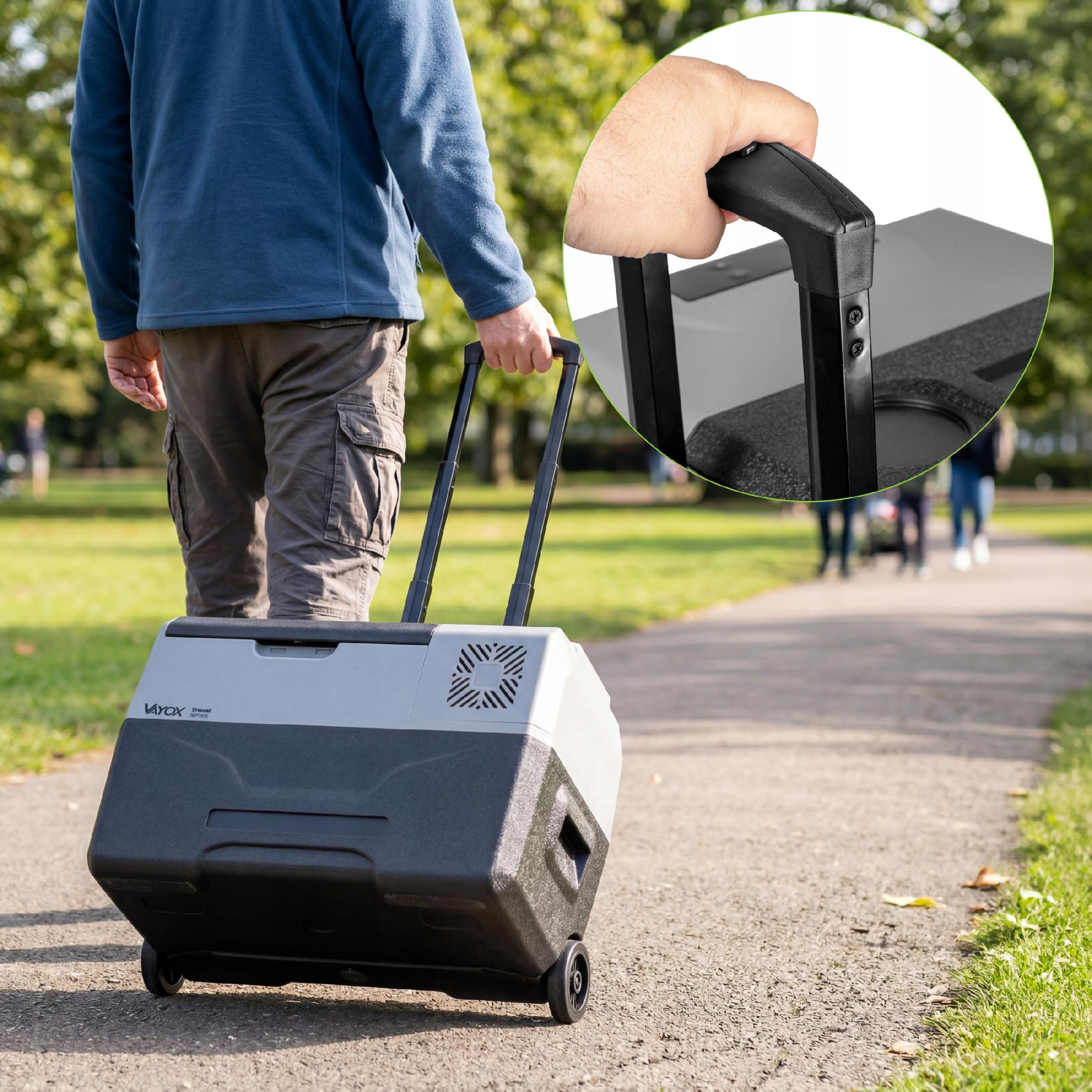 Mann zieht eine graue und schwarze Kühlbox mit Rollen auf einem Weg.