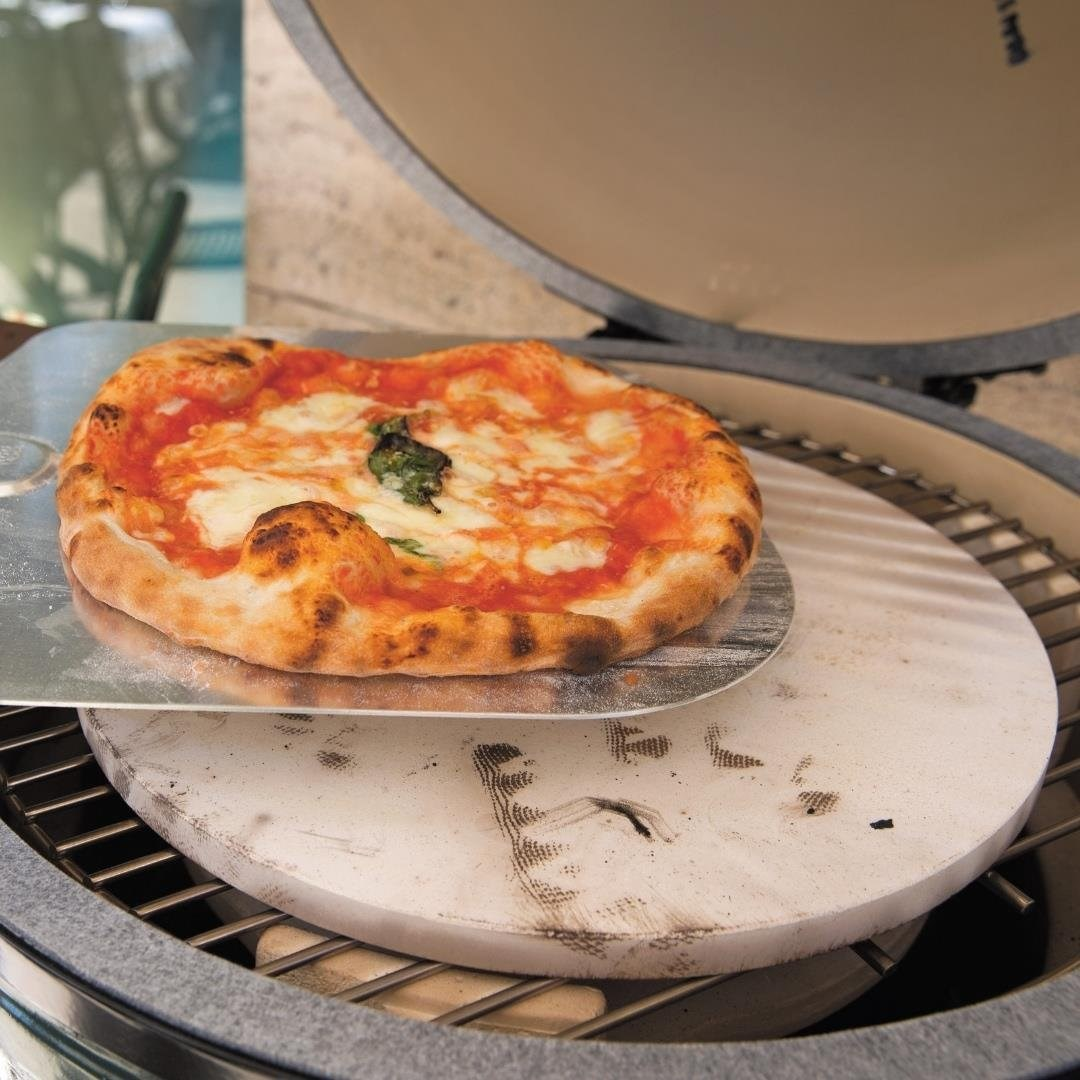 Kırmızı soslu ve beyaz peynirli taze pişmiş pizza, taşın üzerindeki pizza küreği üzerinde duruyor.