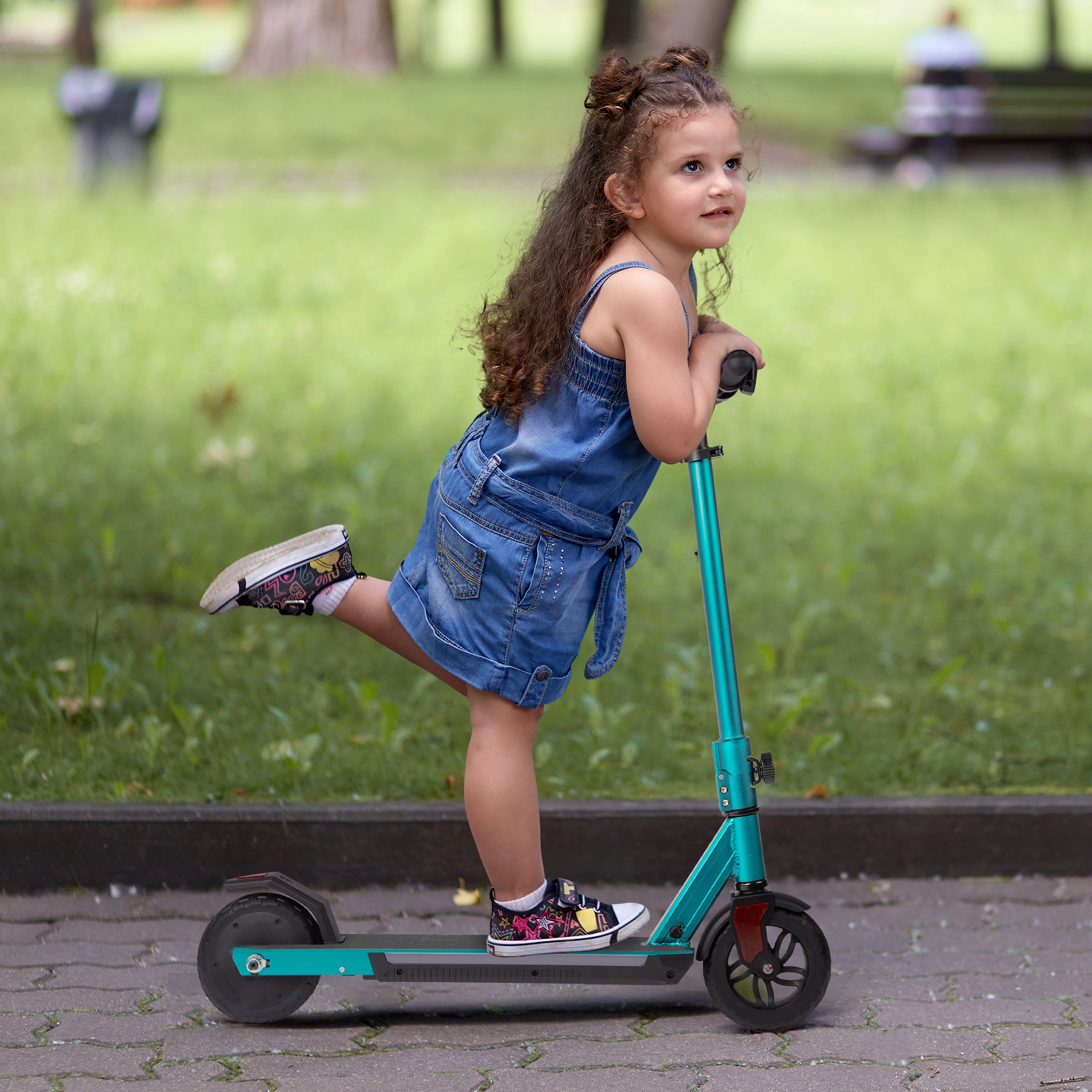 Ein kleines Mädchen in einem Jeans-Overall fährt auf einem blauen Roller im Park.