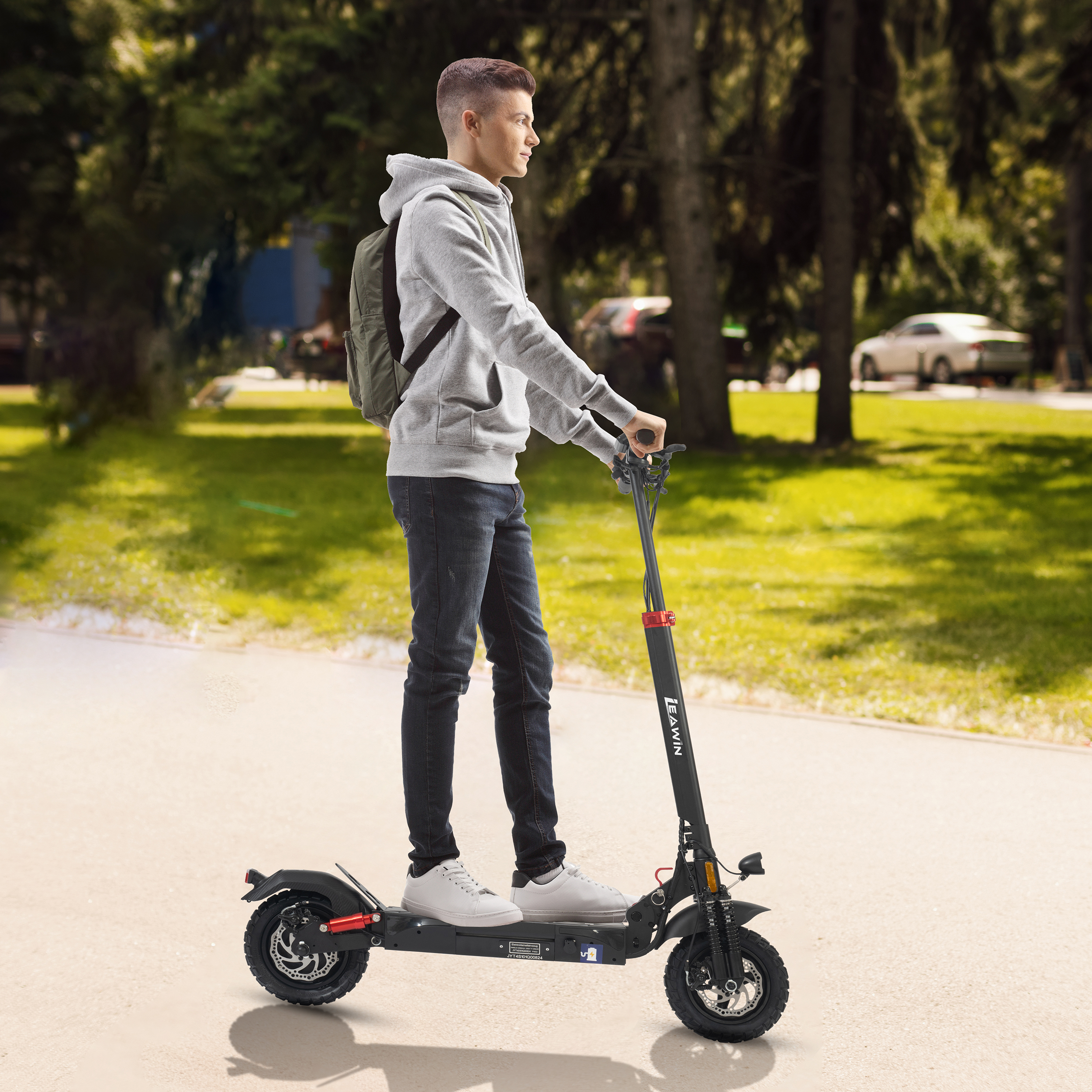 Ein junger Mann fährt einen schwarzen Elektroroller auf einem Weg im Park.